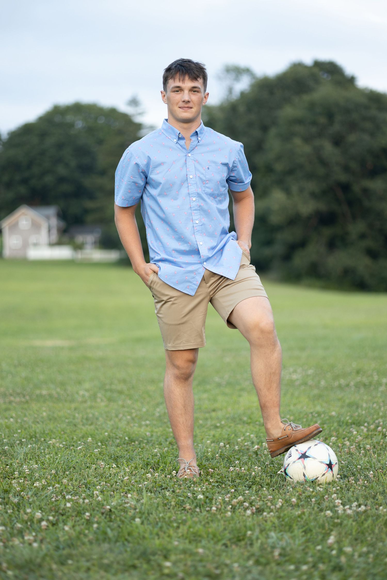 Person in casual attire posing with soccer ball on grassy field.