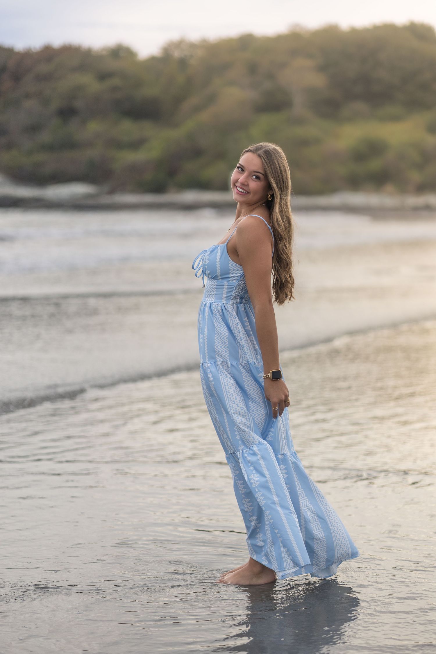 Sunset beach photoshoot featuring a flowing light blue dress with water in the background.