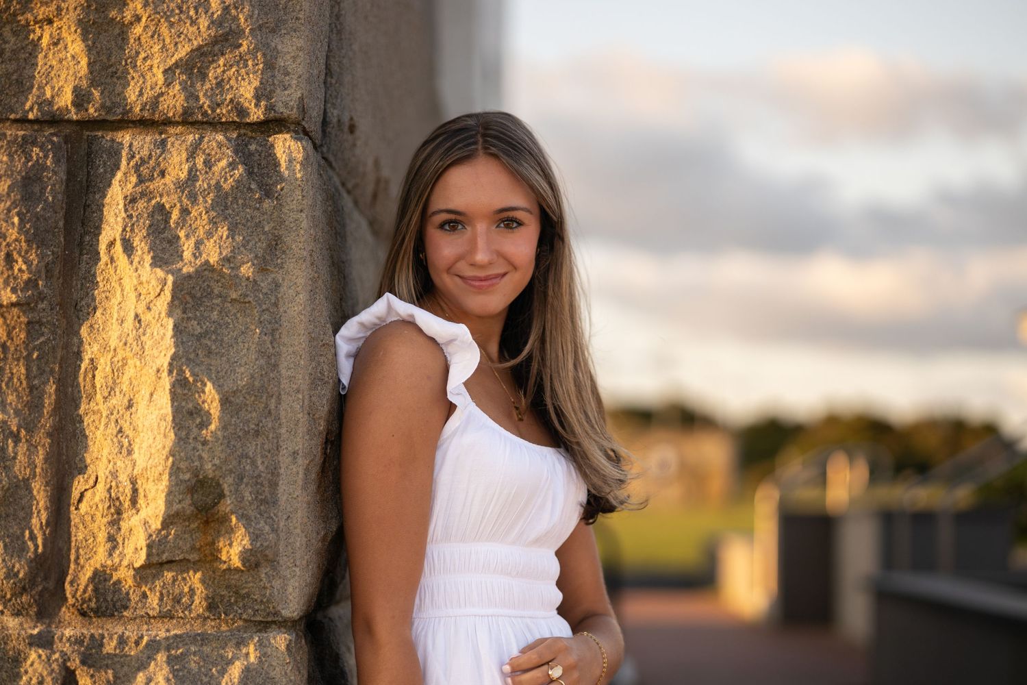 Woman in white dress leans against stone pillar during golden hour portrait session.