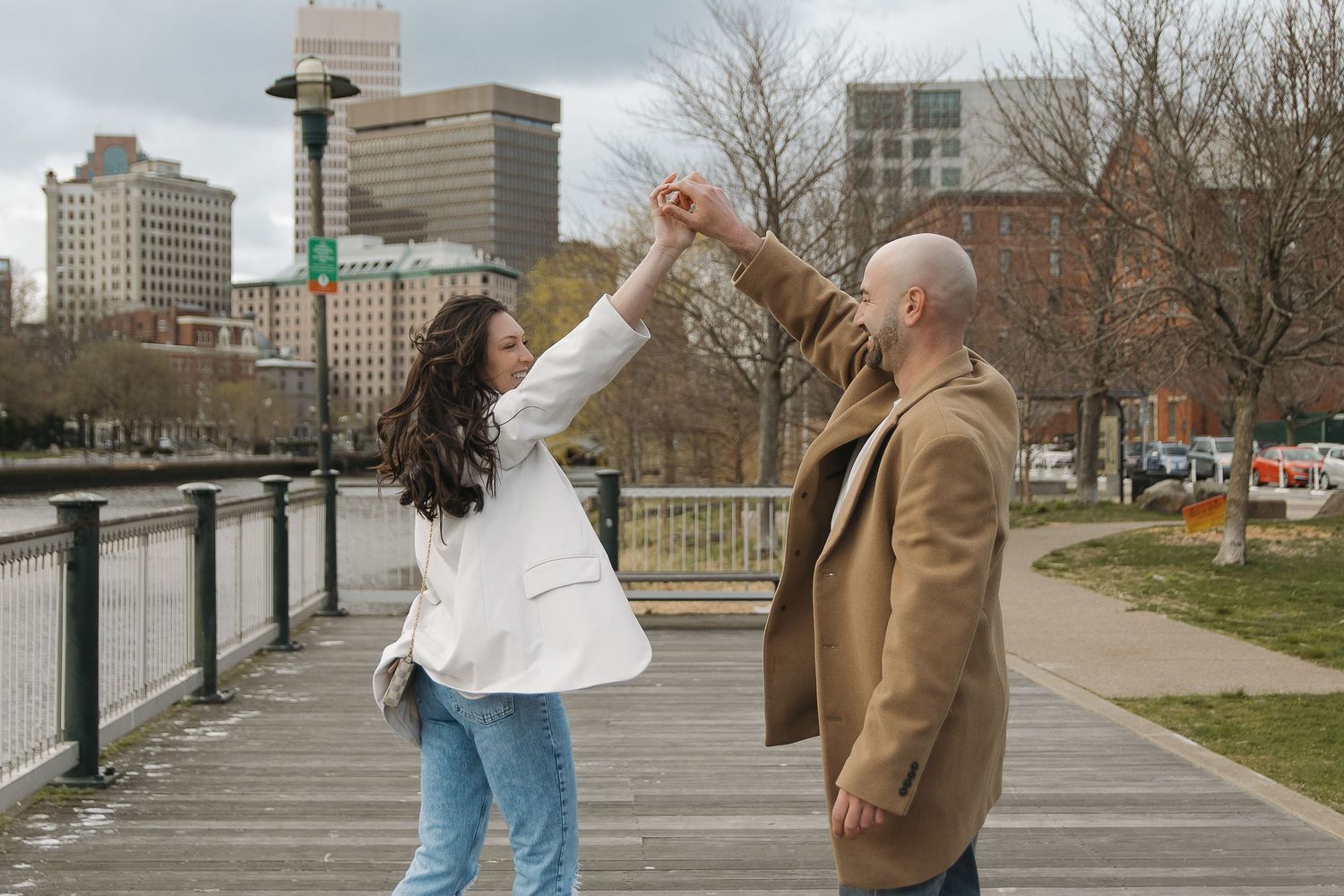 Couple dancing together on boardwalk with city buildings in background.