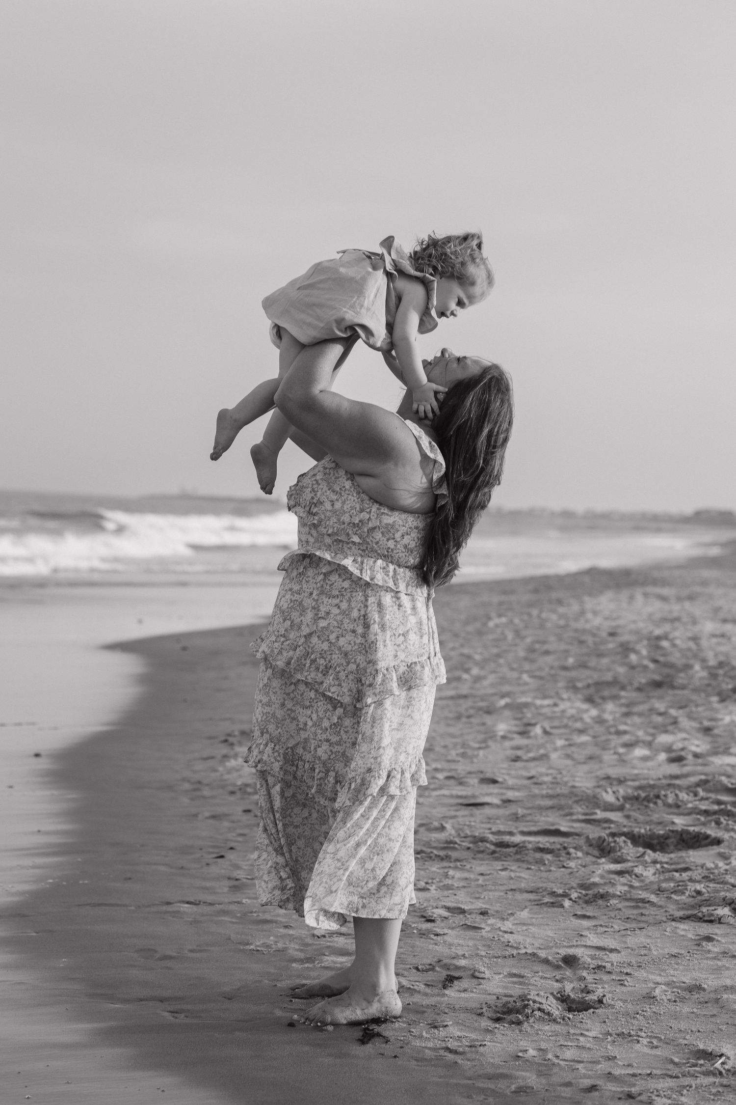 Black and white portrait of parent and child sharing joyful moment on beach.