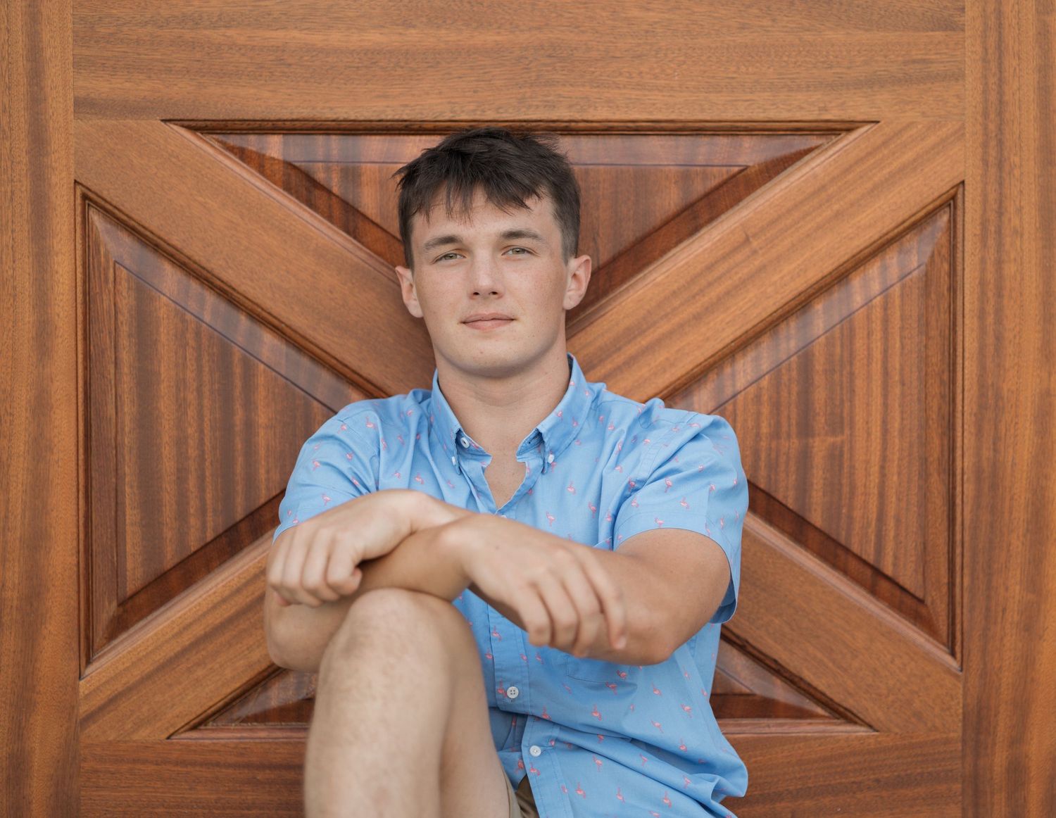 A person wearing a light blue button-down shirt sits on wooden stairs with geometric patterns in the background.