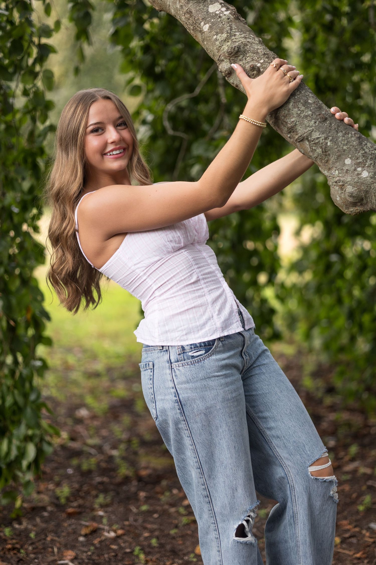Casual summer outfit with white top and distressed jeans posed by a tree in a garden setting.