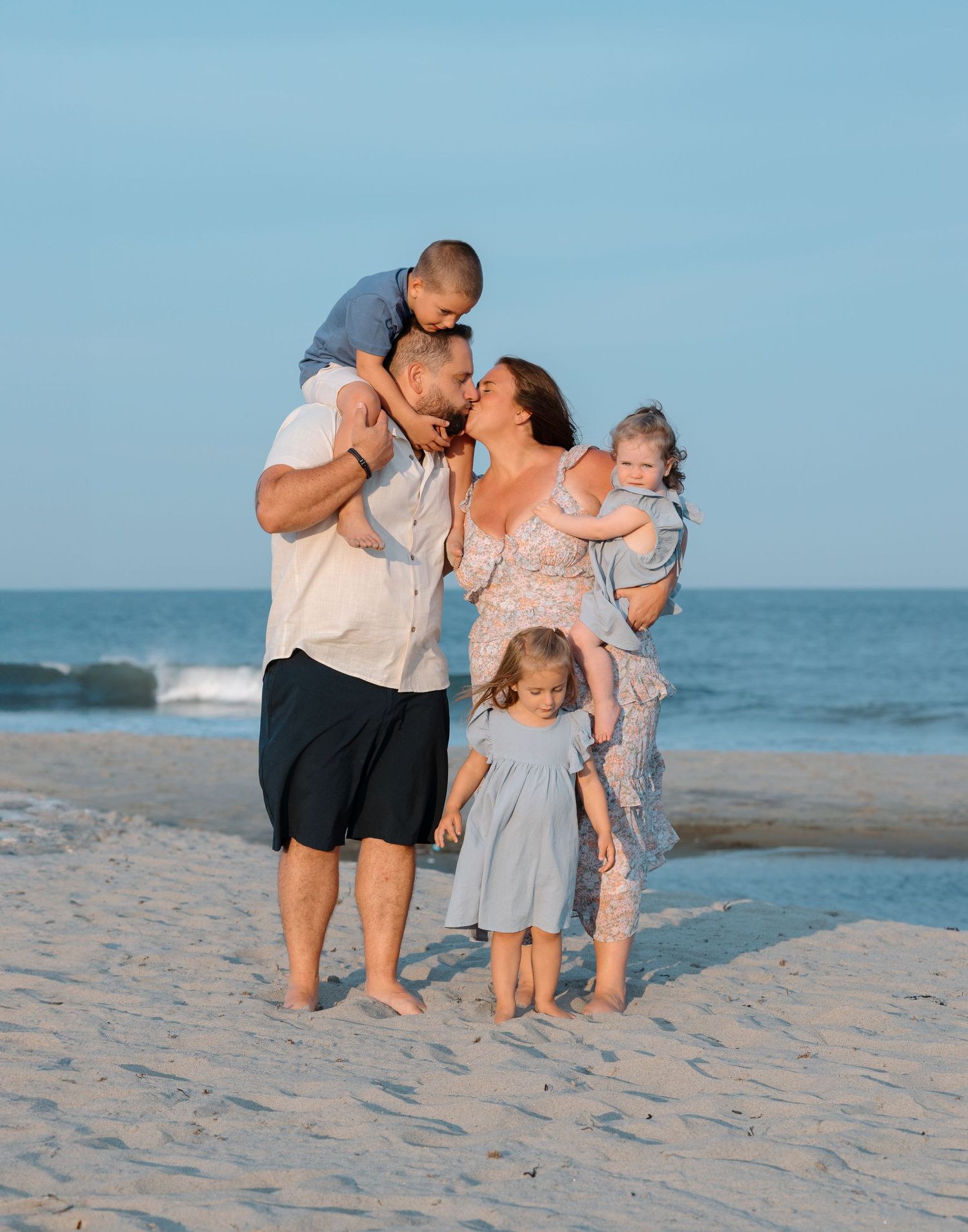 Family sharing playful moments together on beach with ocean waves in background.