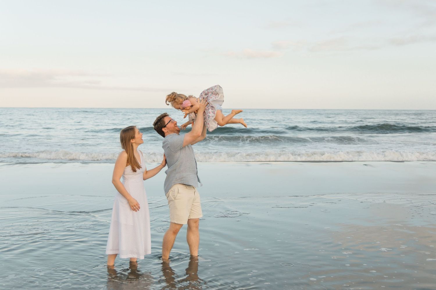 Joyful family moment on the beach at sunset with ocean waves in the background.