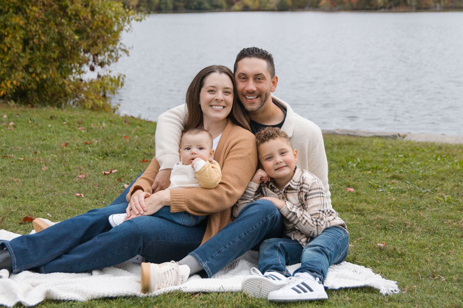 A family relaxes on a blanket by a lake during fall season.