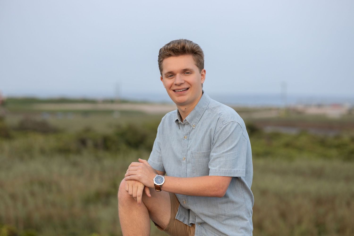 A casual portrait in front of a coastal landscape with cloudy skies.