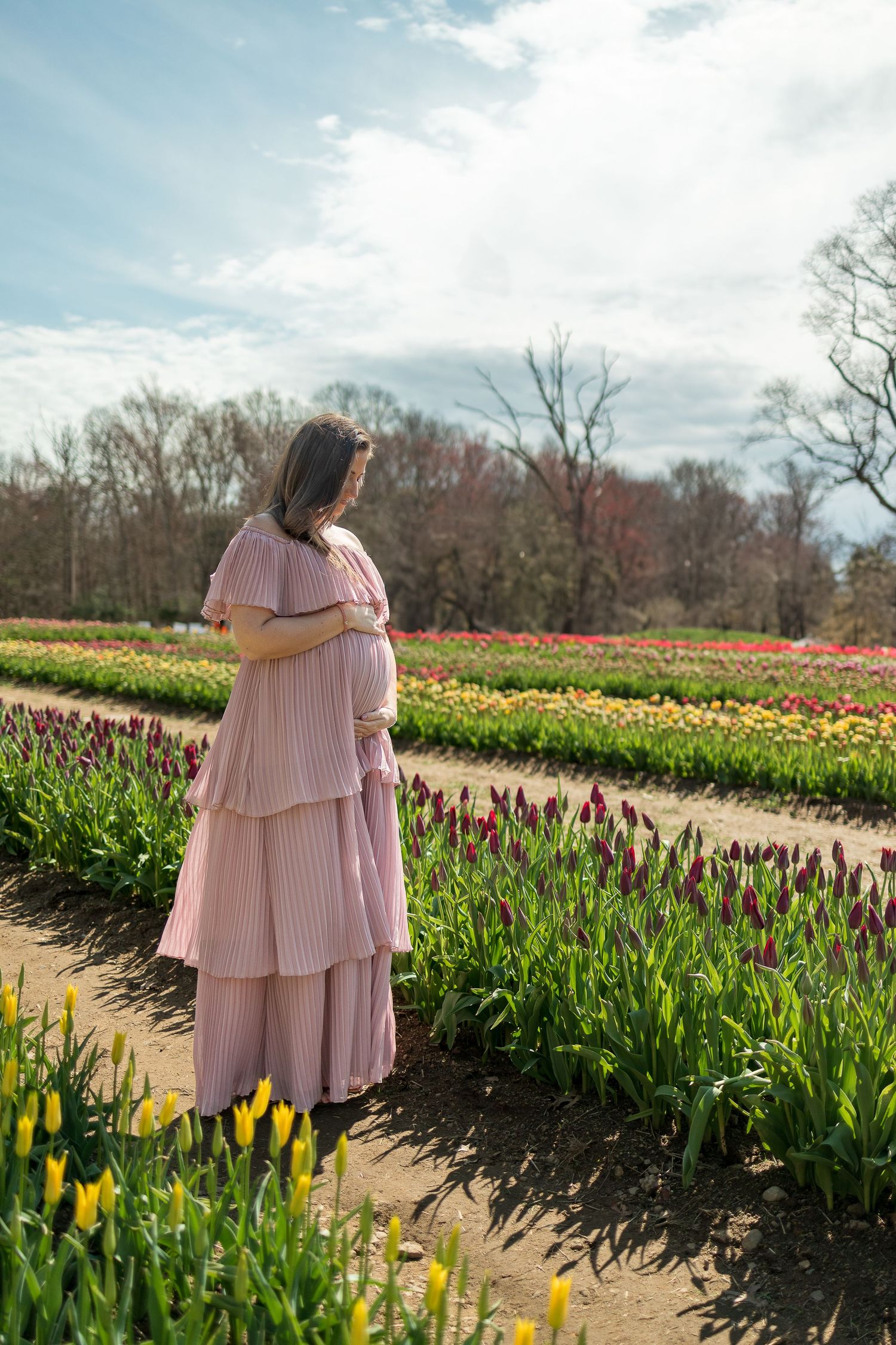 Woman in pink tiered dress standing among rows of colorful spring tulips.