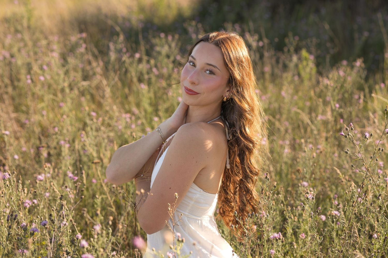 A figure in a white dress poses gracefully in a sunlit meadow during golden hour.