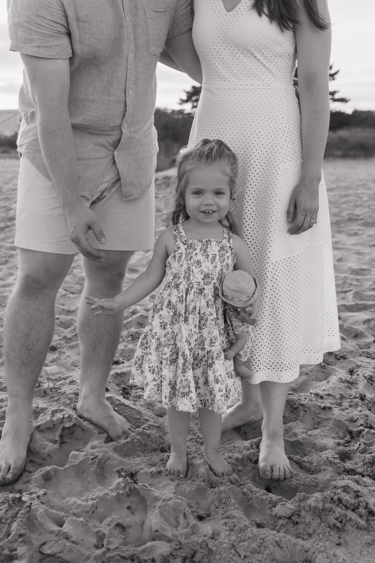 A black and white portrait of a family standing barefoot in the sand at the beach.
