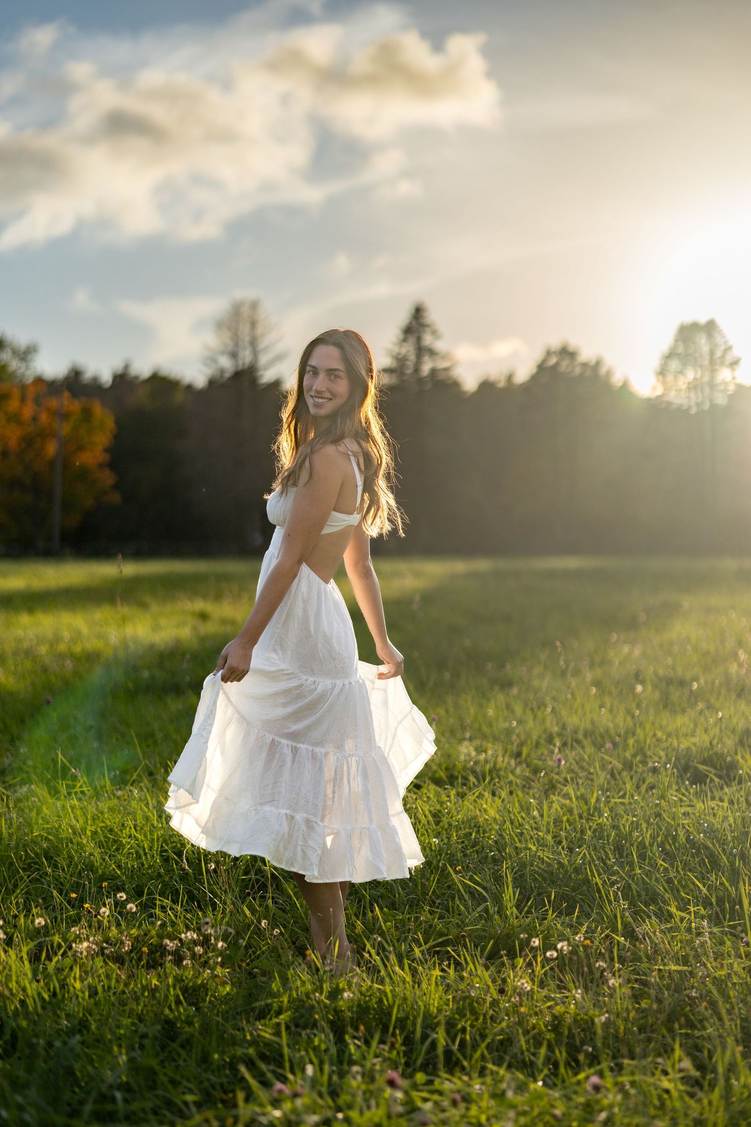 A person in a flowing white dress twirls in a sunlit meadow at golden hour.