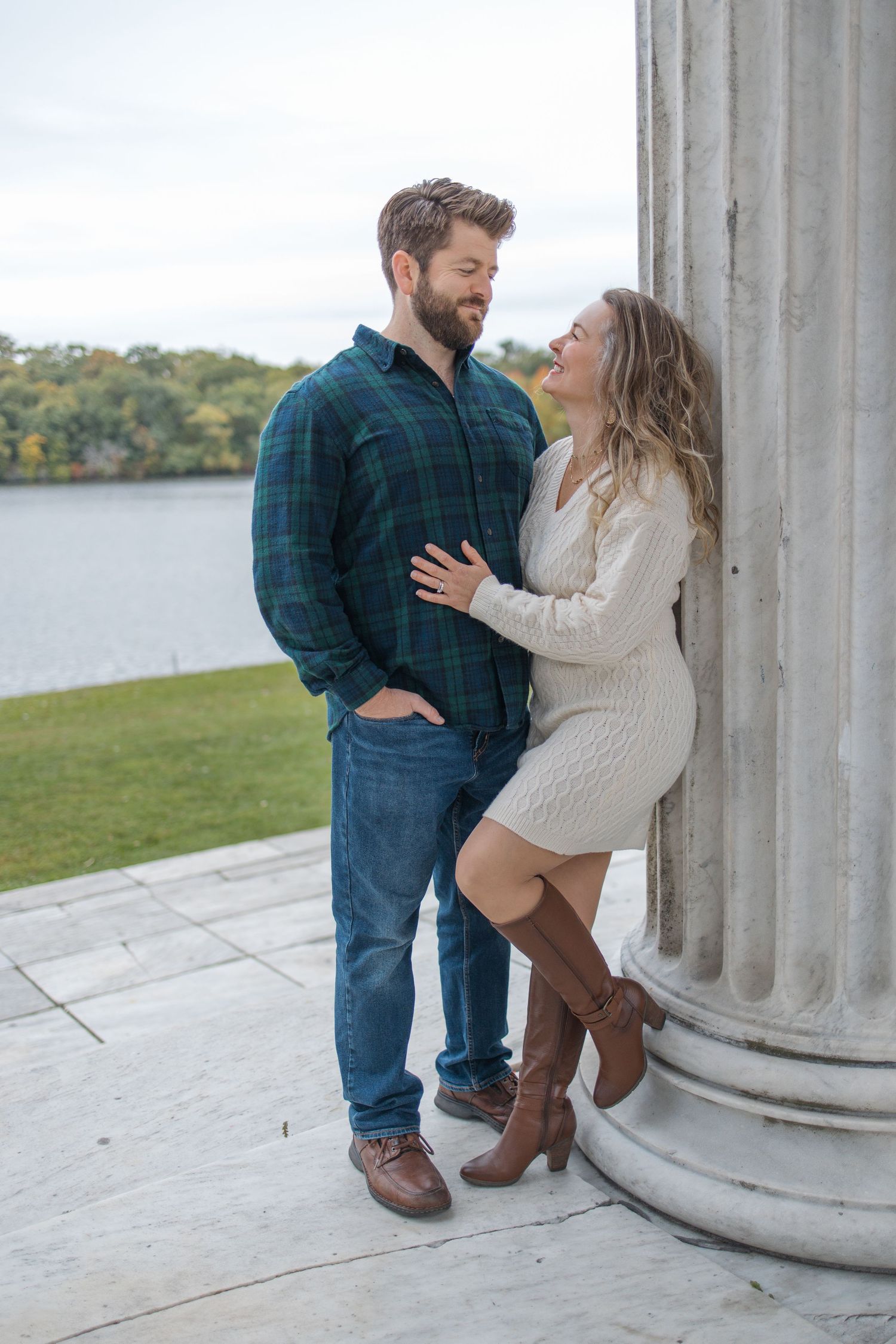 A couple shares a romantic moment by a classical column overlooking a lake.