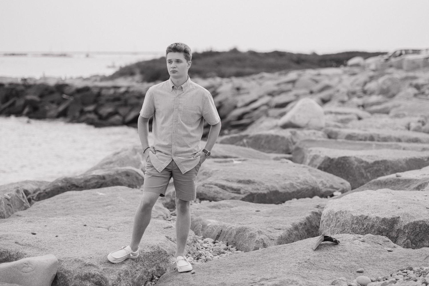Black and white photo of someone standing on rocky coastal terrain.