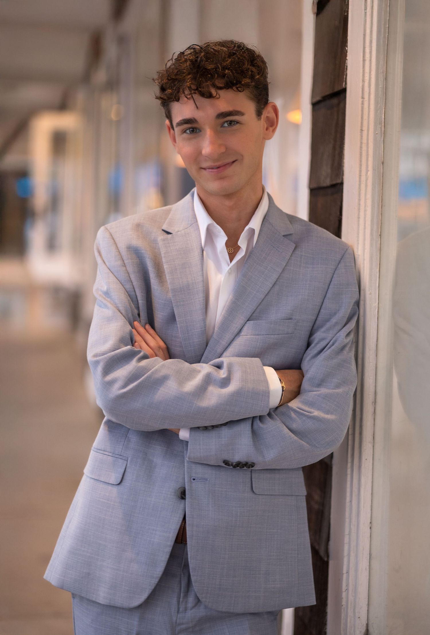 A person in a light gray suit jacket poses casually against a white wall in a series of connected photos.