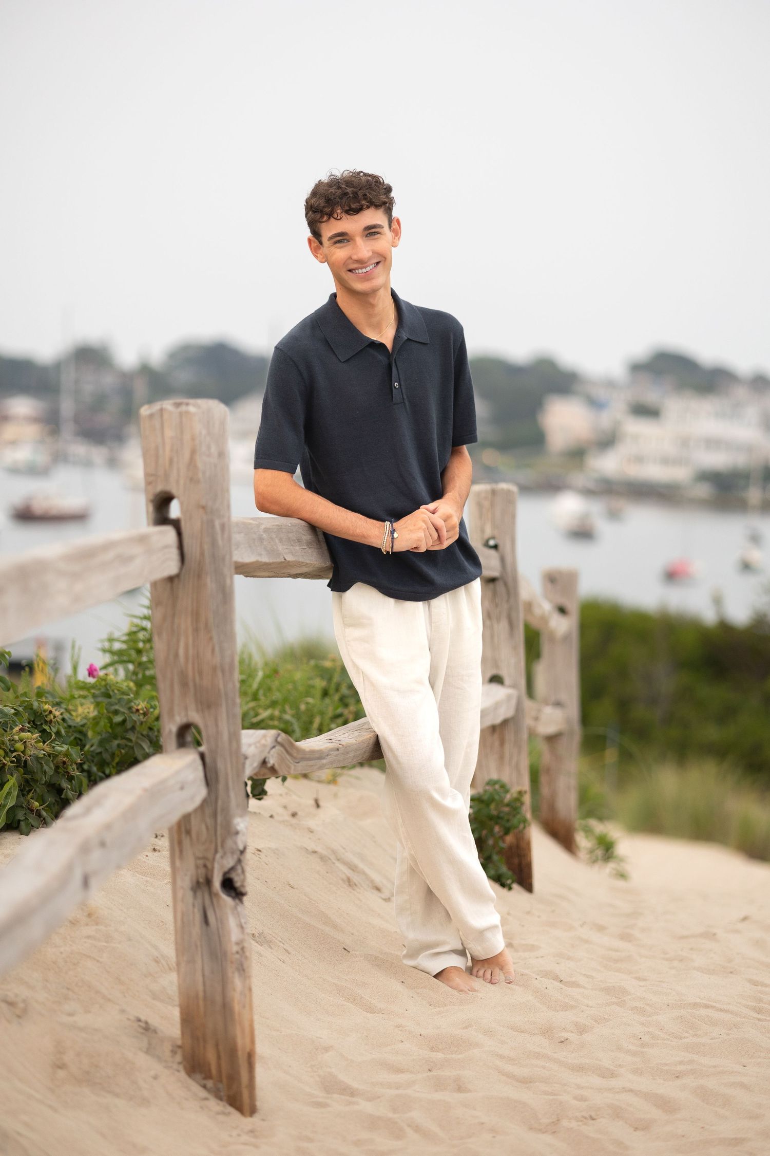 Casual summer portrait on wooden fence overlooking harbor with boats in background.