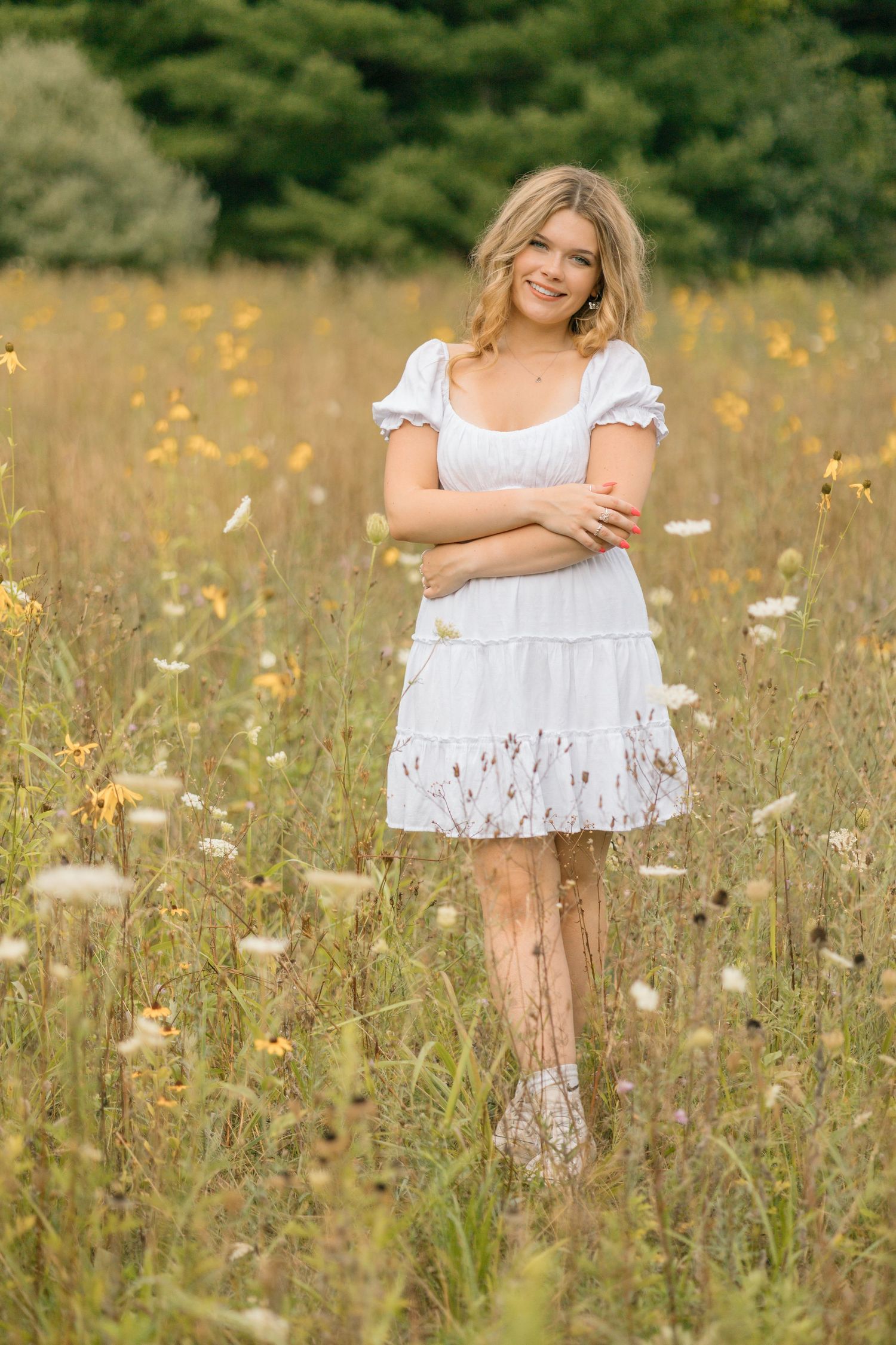 A casual summer portrait in a white dress surrounded by tall grass and yellow wildflowers.