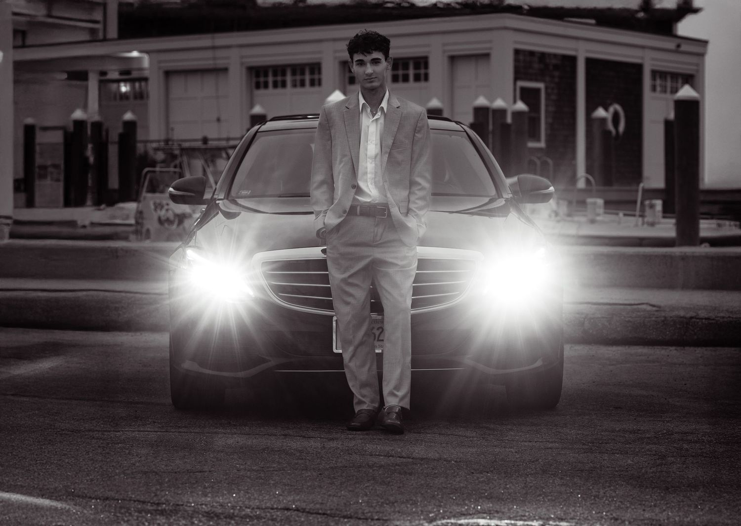 Black and white photo of someone standing in front of a car with bright headlights illuminated at night.