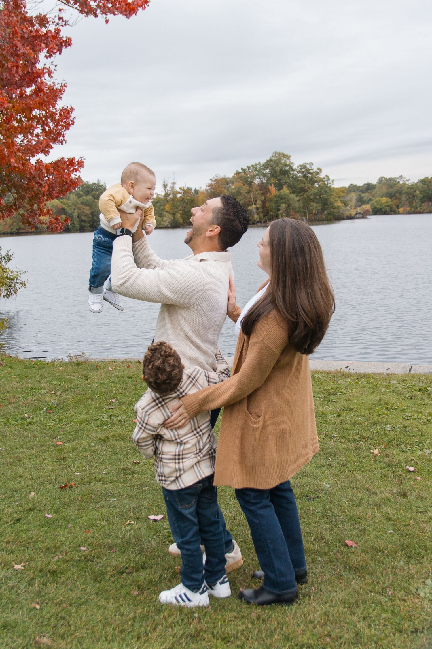 A family enjoying an autumn day by a lake with fall foliage in the background.