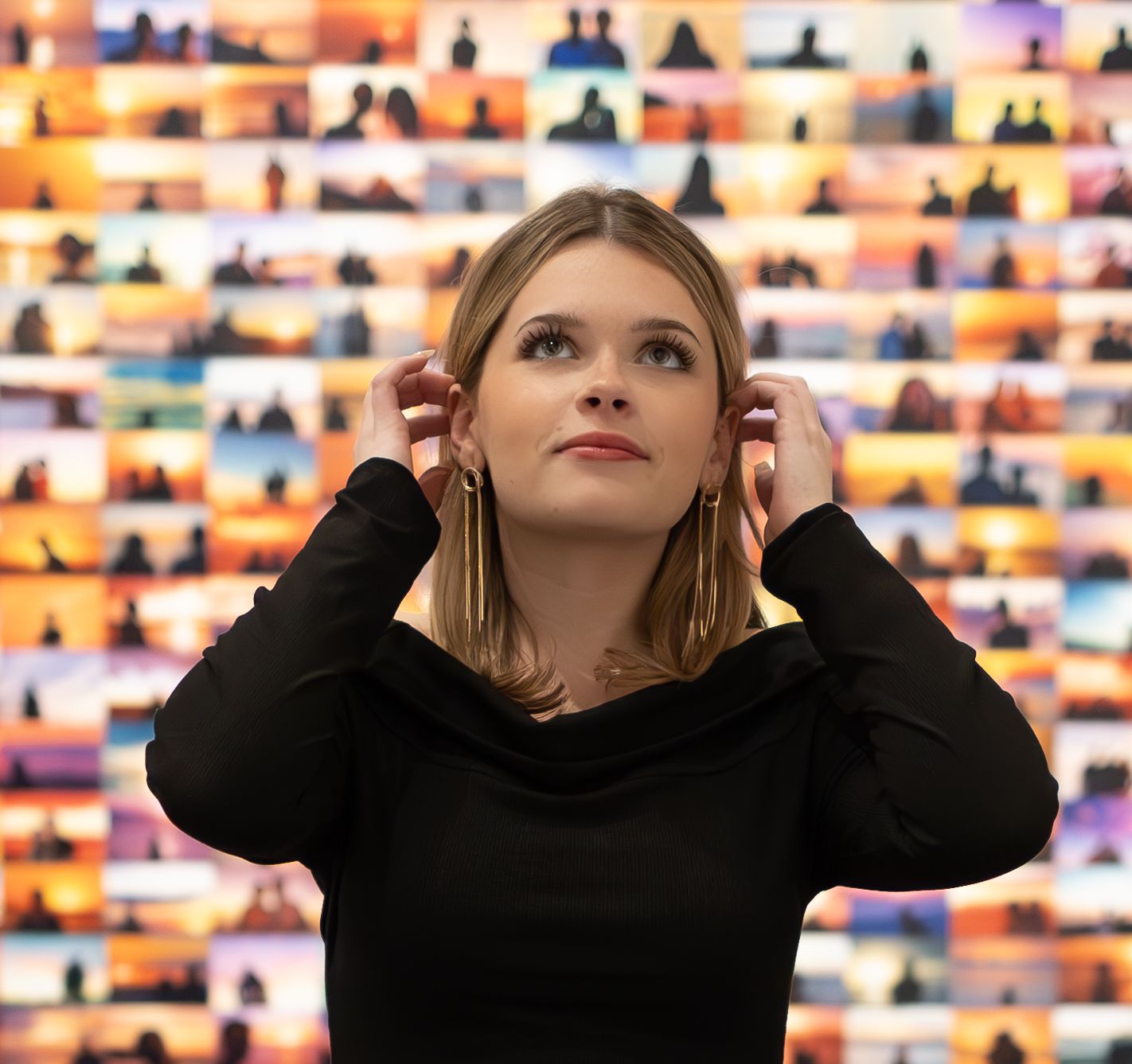 A person in black adjusting headphones against a colorful wall display of illuminated panels.