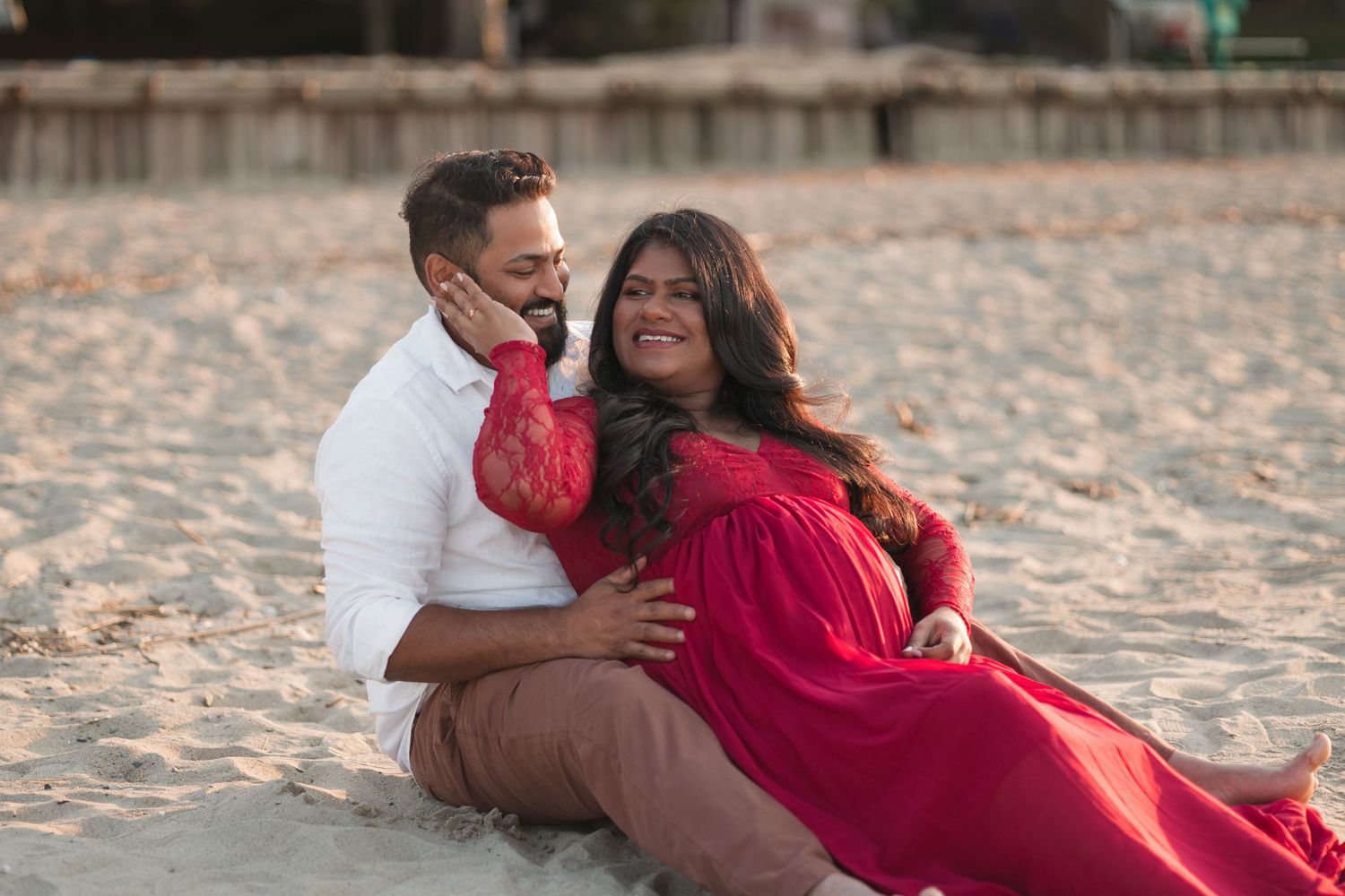 Couple in white and red outfits share romantic moment on sandy beach.