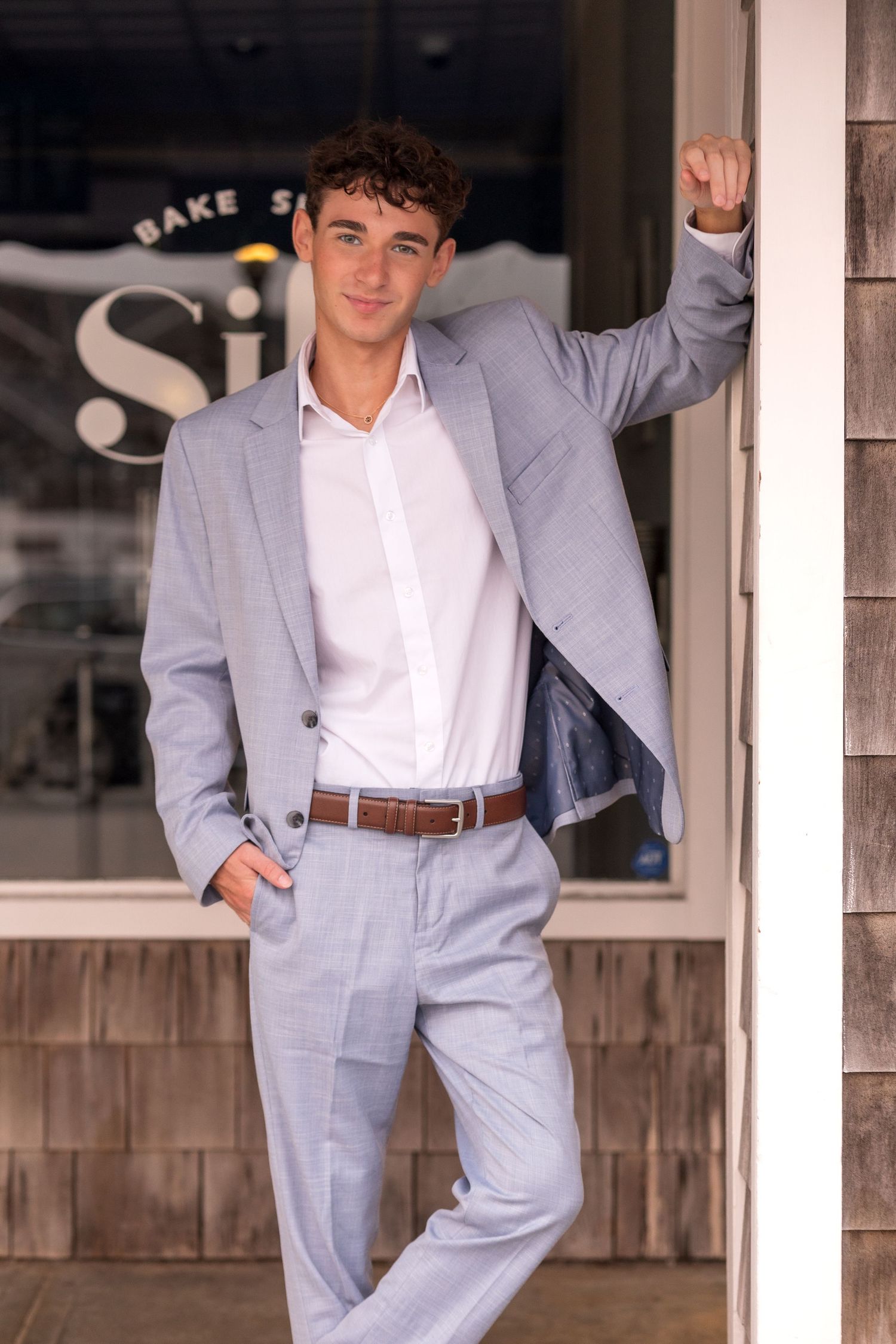 A person in a light gray suit and white shirt poses against a wooden wall in multiple casual stances.