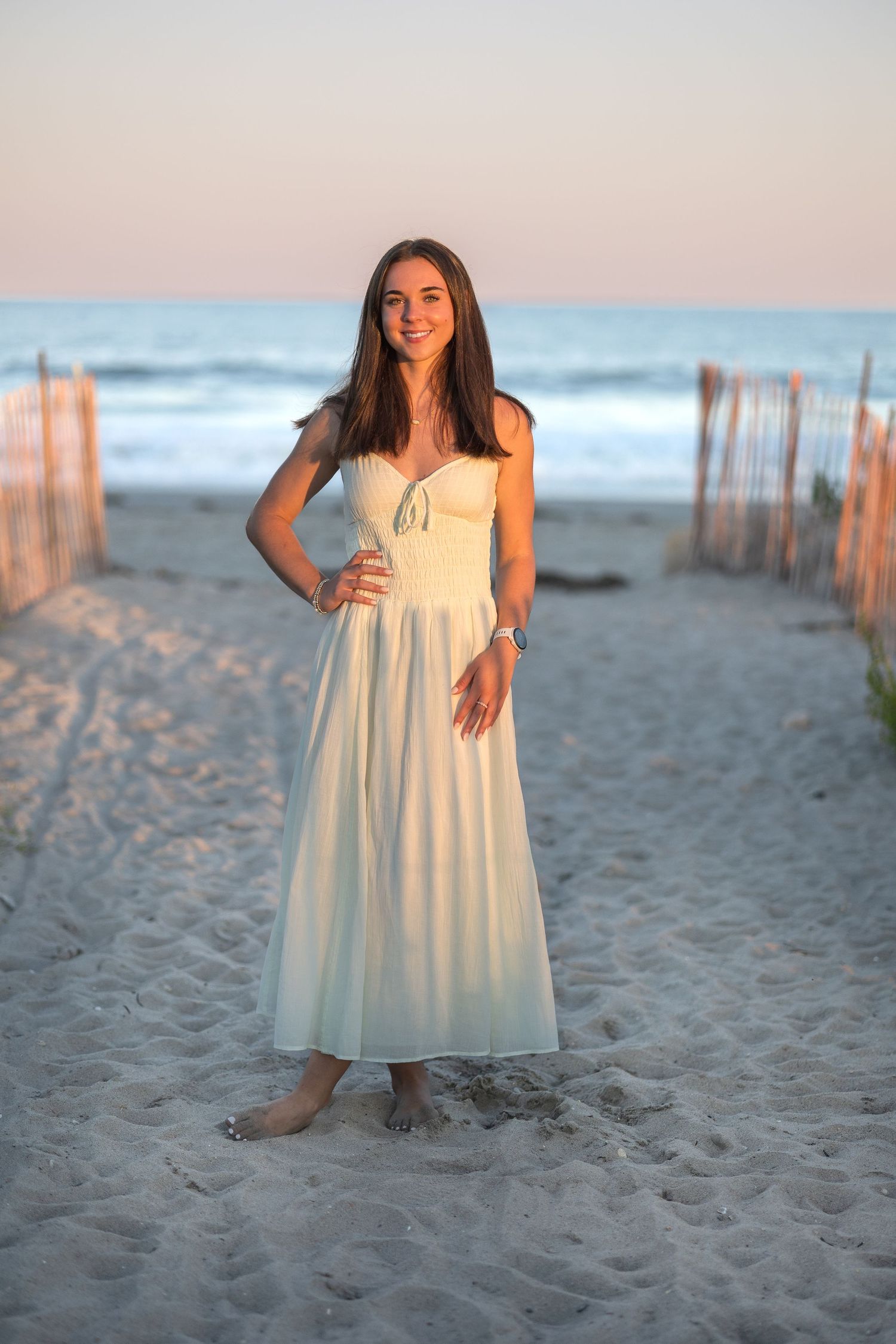 White summer dress on sandy beach at sunset with wooden posts in background.