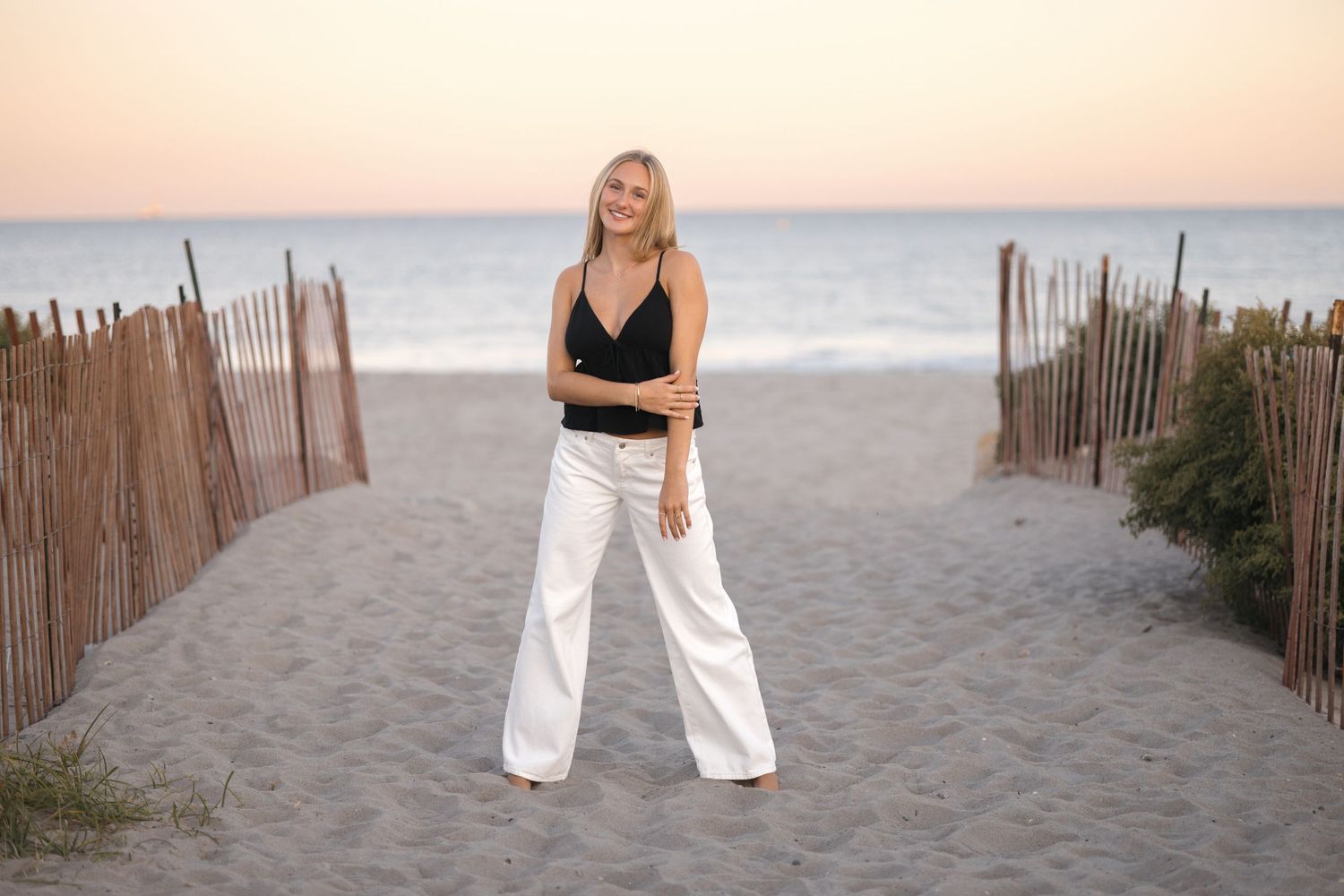 Fashion photo on sandy beach path with wooden fencing at dusk.