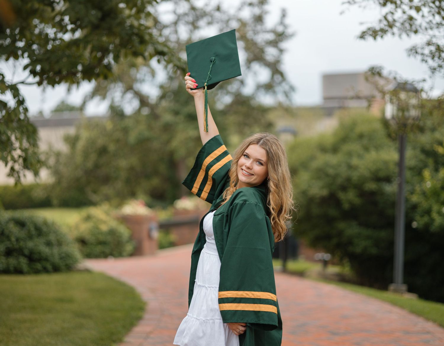 A graduate celebrates by raising their cap high while wearing traditional green graduation regalia.