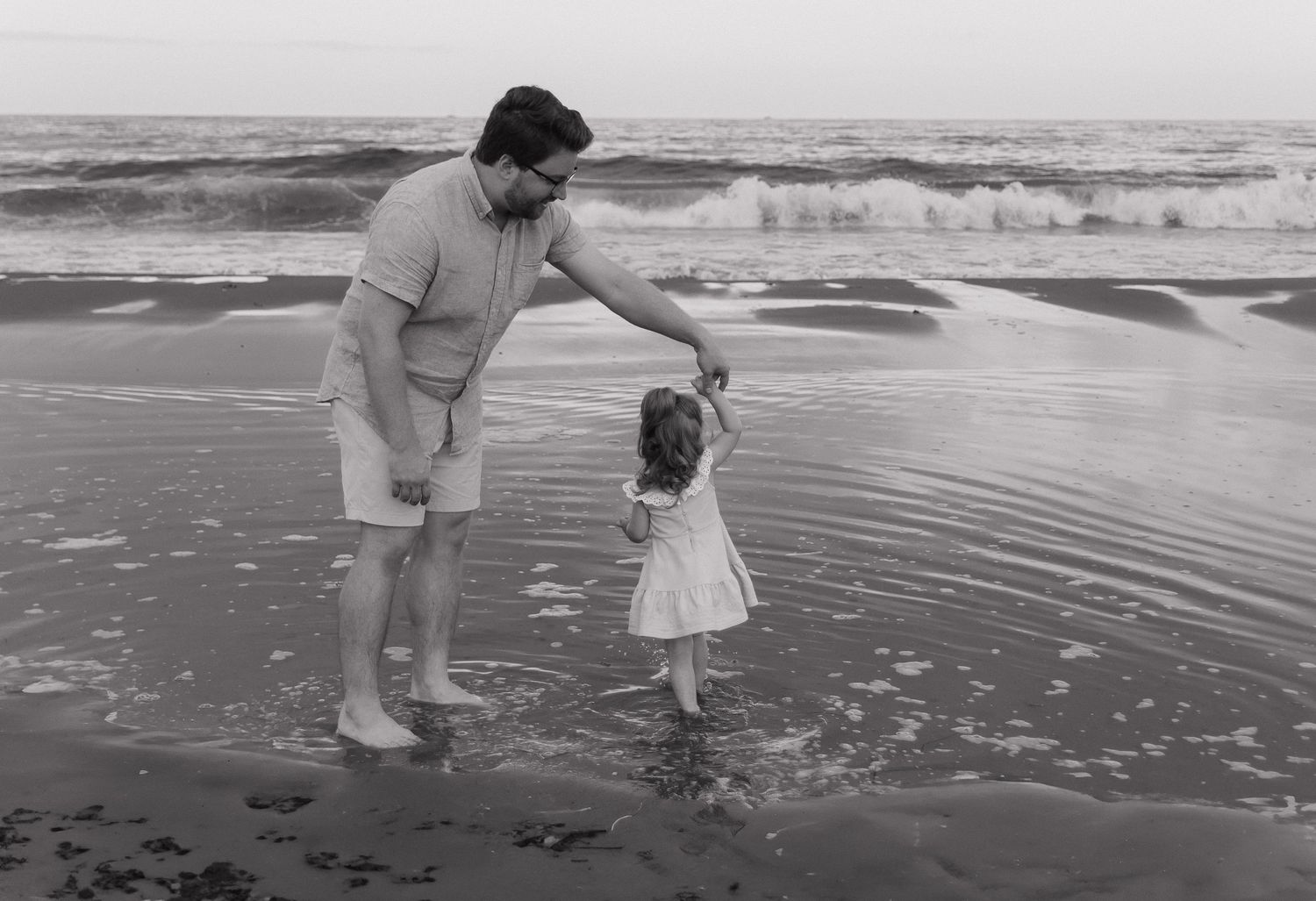 A black and white image of a parent and child playing on the beach.