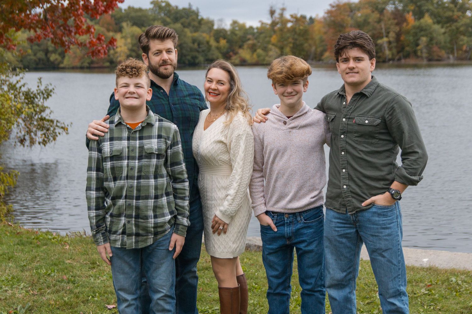 Group portrait by a lake during fall with autumn foliage in the background.