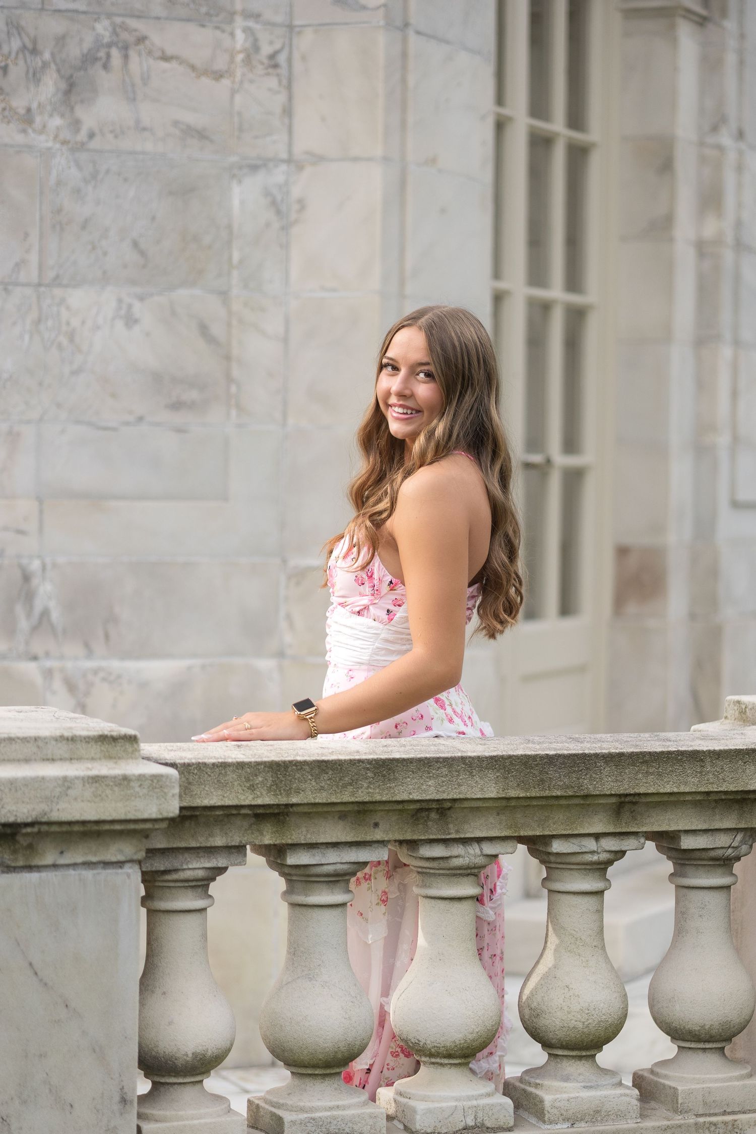A pink floral dress is photographed against a classic stone balustrade with architectural details.