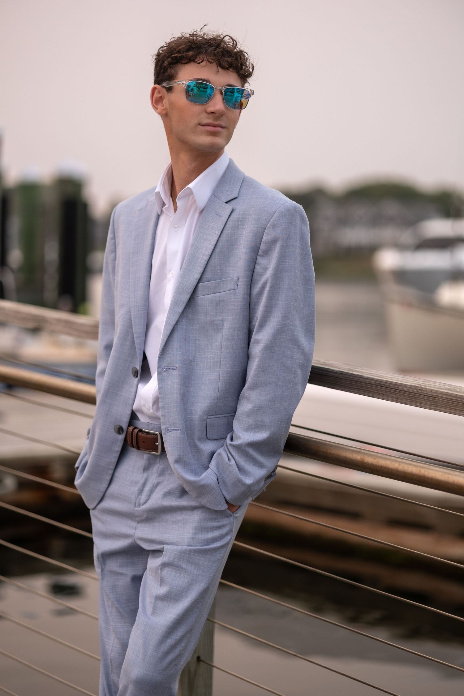 A person in a light gray suit and sunglasses poses against a modern architectural backdrop in multiple shots.
