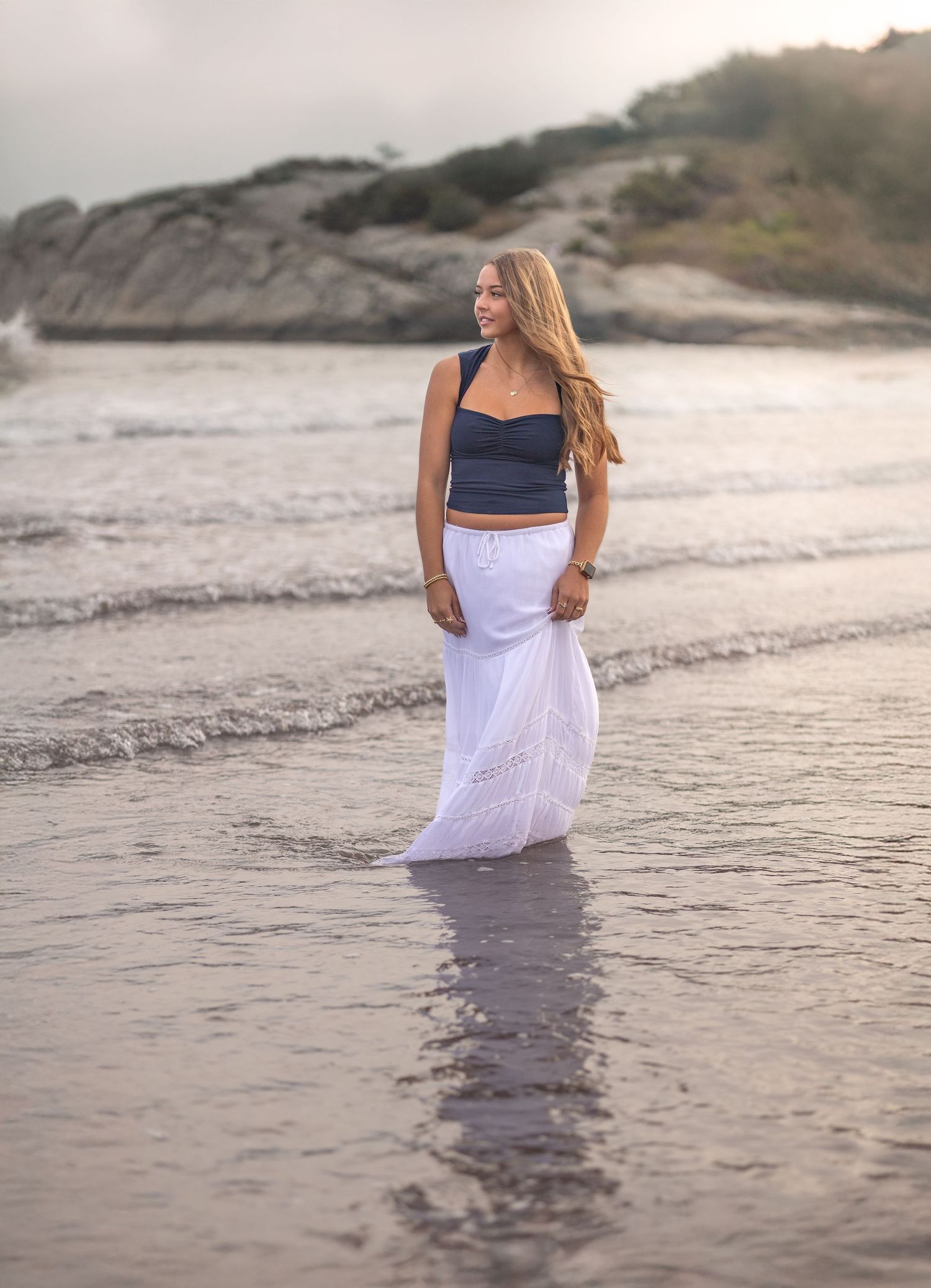 A person in a white dress walks along the shoreline at sunset creating a series of dreamy beach photos.