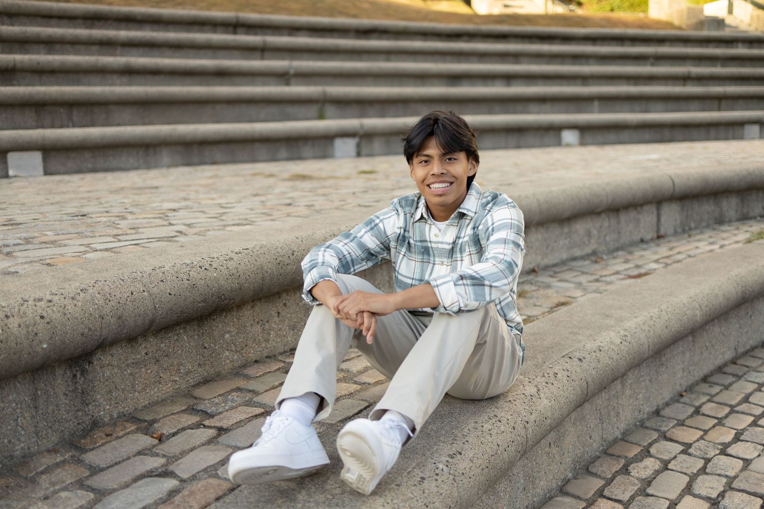 Casual photo of person sitting on outdoor stone steps in plaid shirt and light pants.