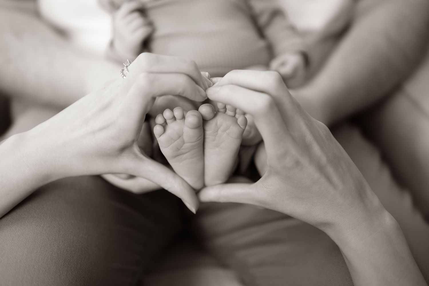 Black and white photo of hands forming heart shape around tiny baby feet.