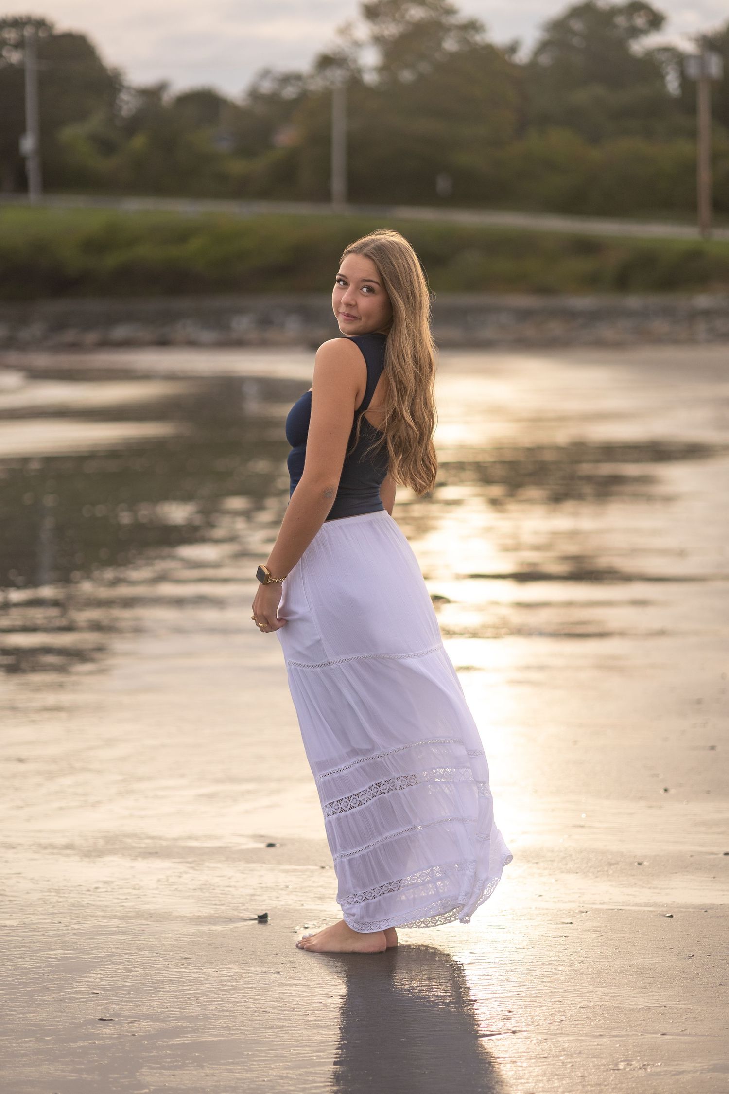 A woman in a white dress twirls playfully on a beach at sunset creating a flowing motion effect.