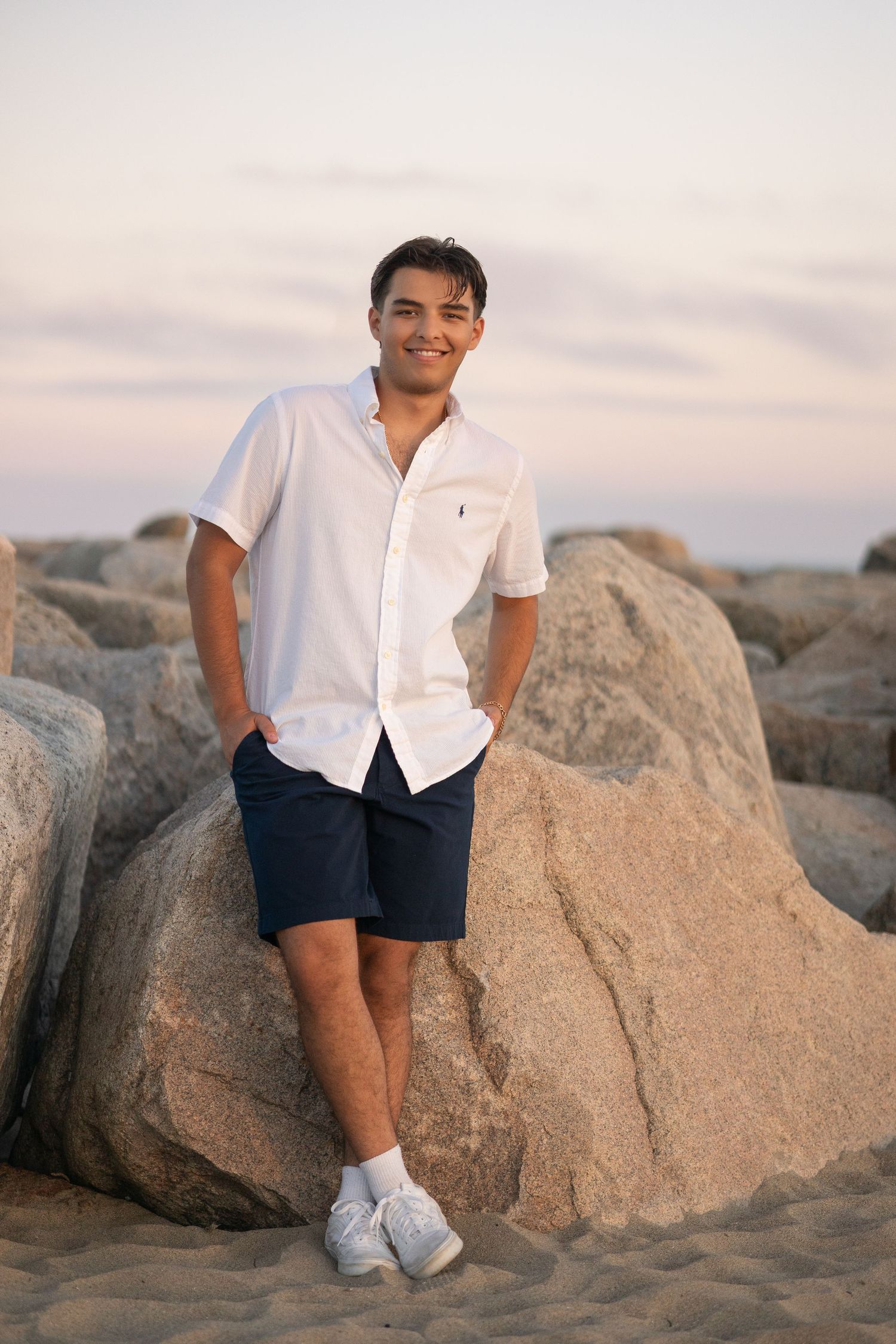 Person sitting casually on coastal rocks wearing a white shirt and navy shorts.