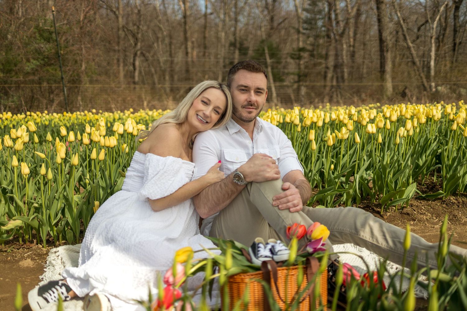 Happy couple enjoying picnic on blanket surrounded by blooming yellow tulips.
