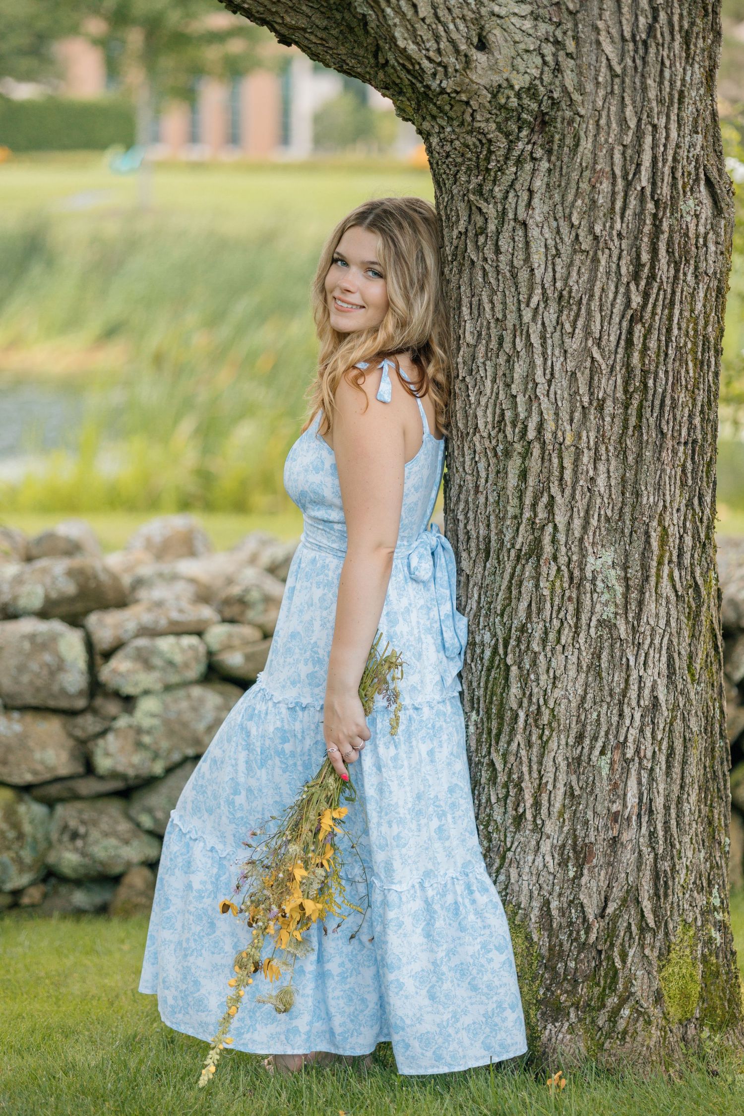 A summer portrait featuring a light blue dress and yellow wildflowers against a large tree trunk.
