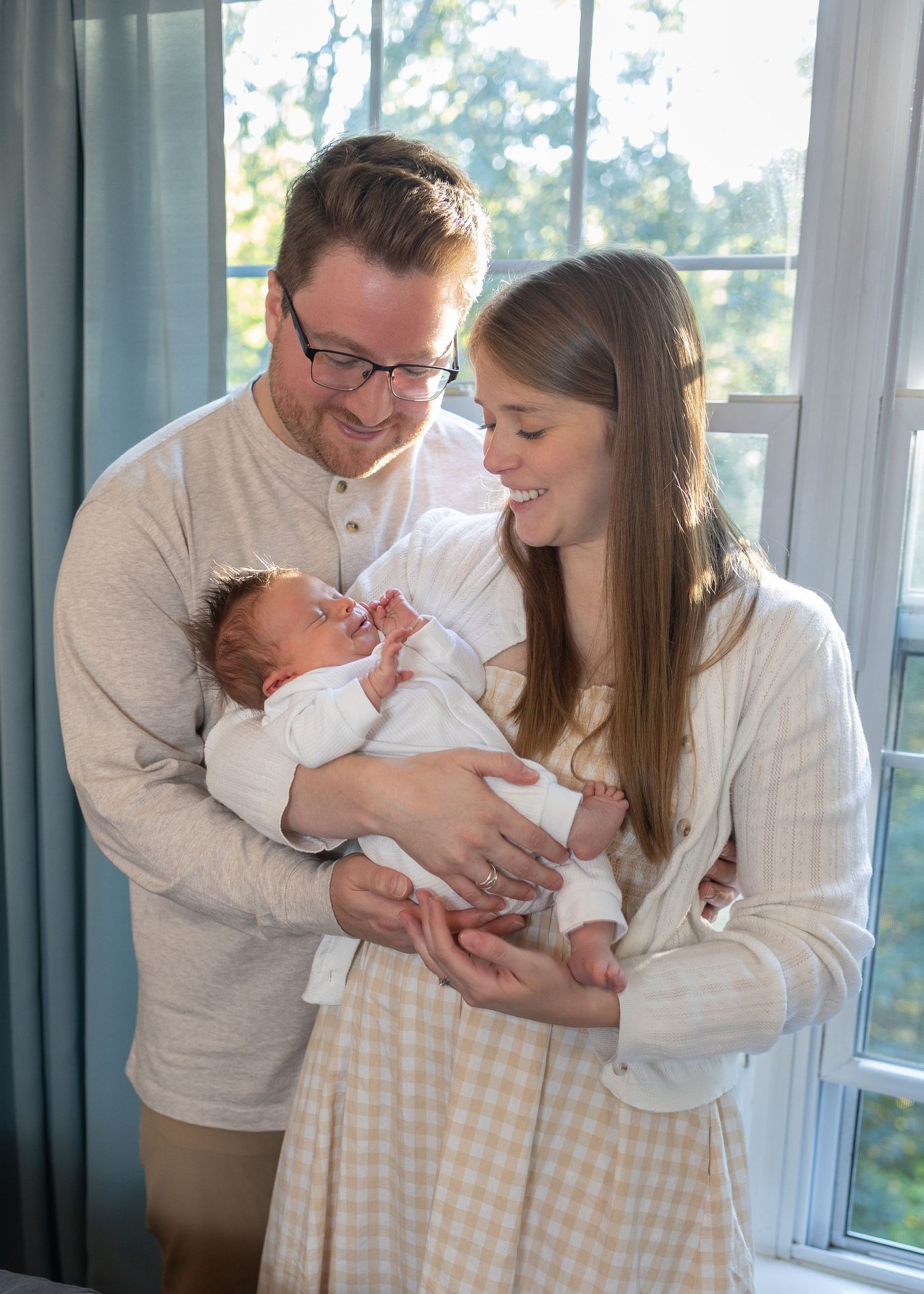 Tender family scene by large windows with blue curtains and natural lighting.