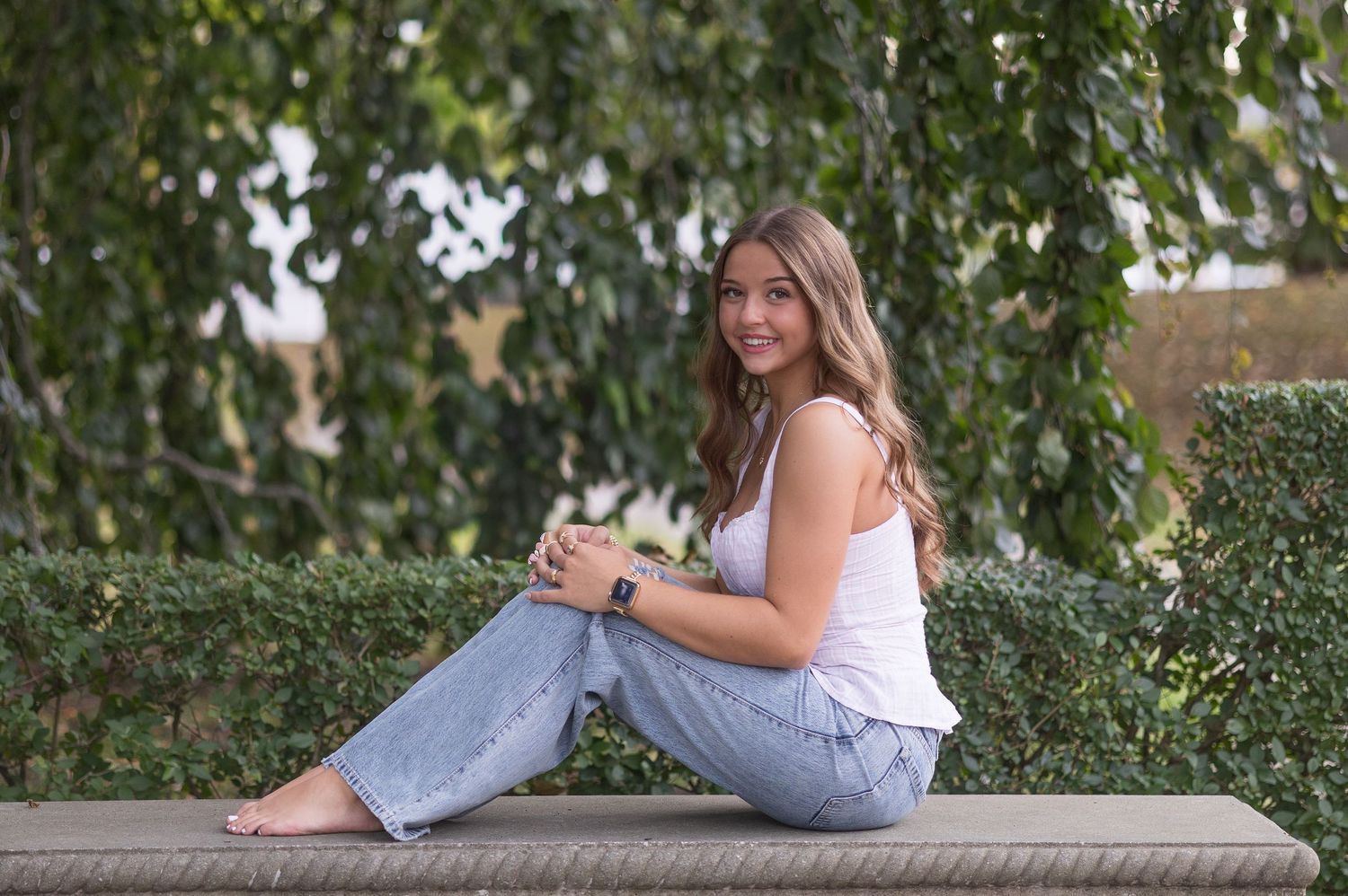 A person in casual attire relaxes on a wooden bench in a lush garden setting.