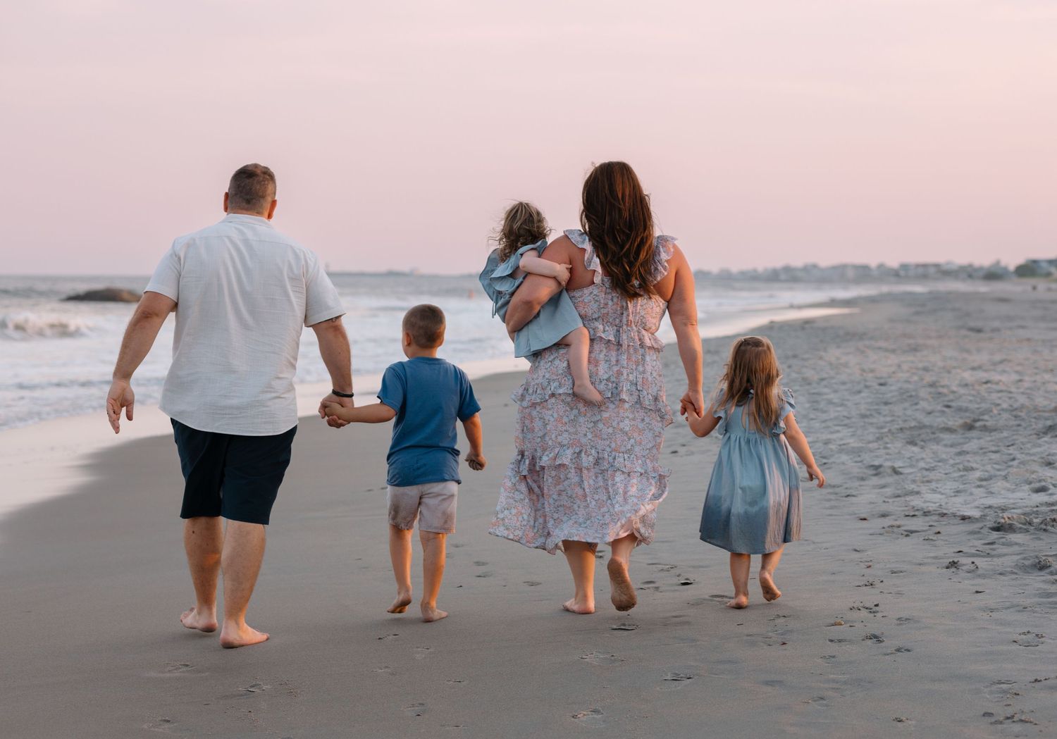 A family walks together along a peaceful beach at sunset holding hands.