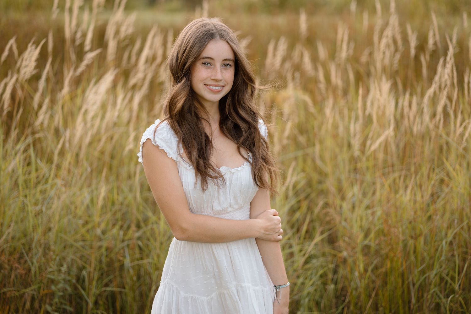 A person in a white dress stands among tall golden grasses during golden hour.