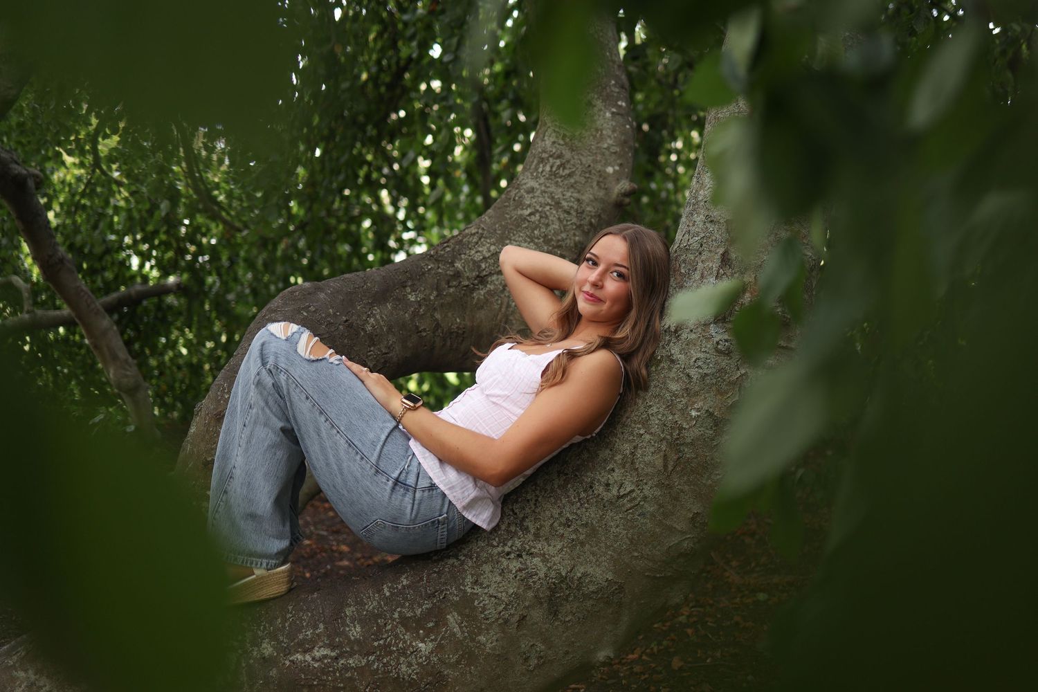 Artistic portrait series taken among tree branches with natural green foliage framing.