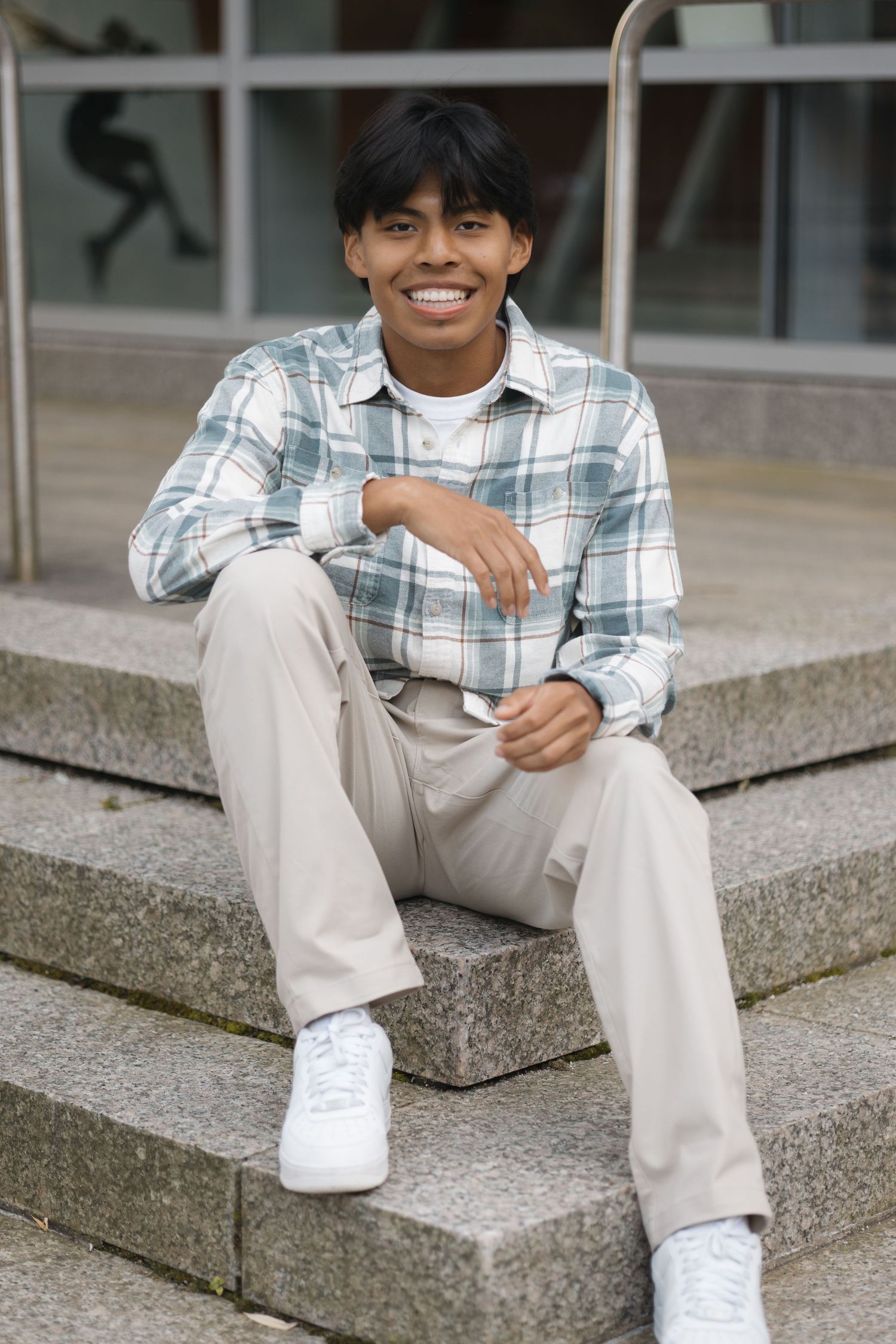 Person sitting on concrete steps wearing plaid shirt and khaki pants with white sneakers.