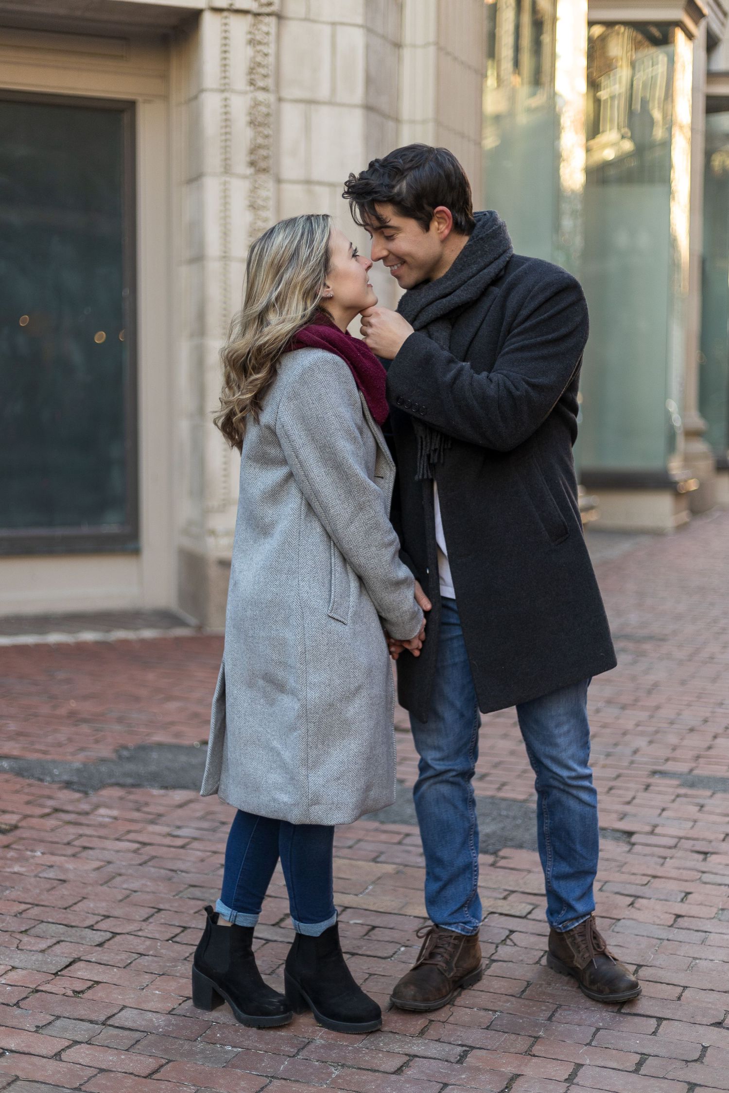 A tender moment shared between a couple on brick pavement in winter attire.