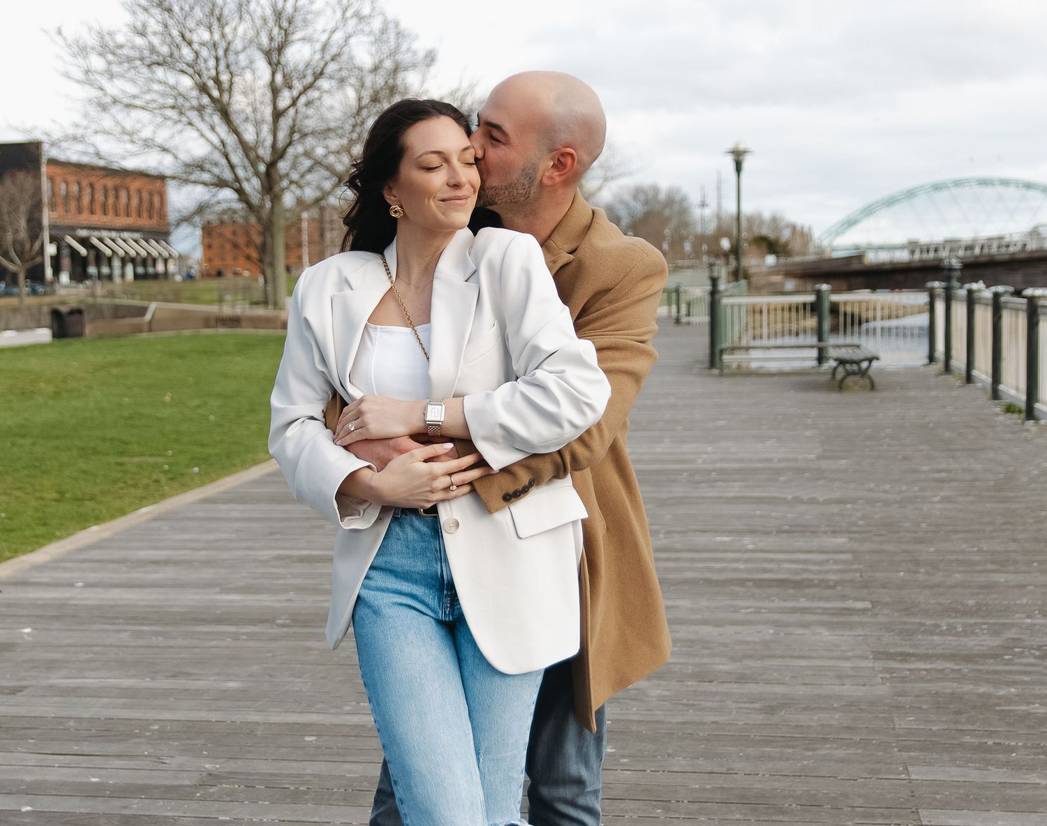 Couple sharing romantic moment on riverside boardwalk in urban setting.