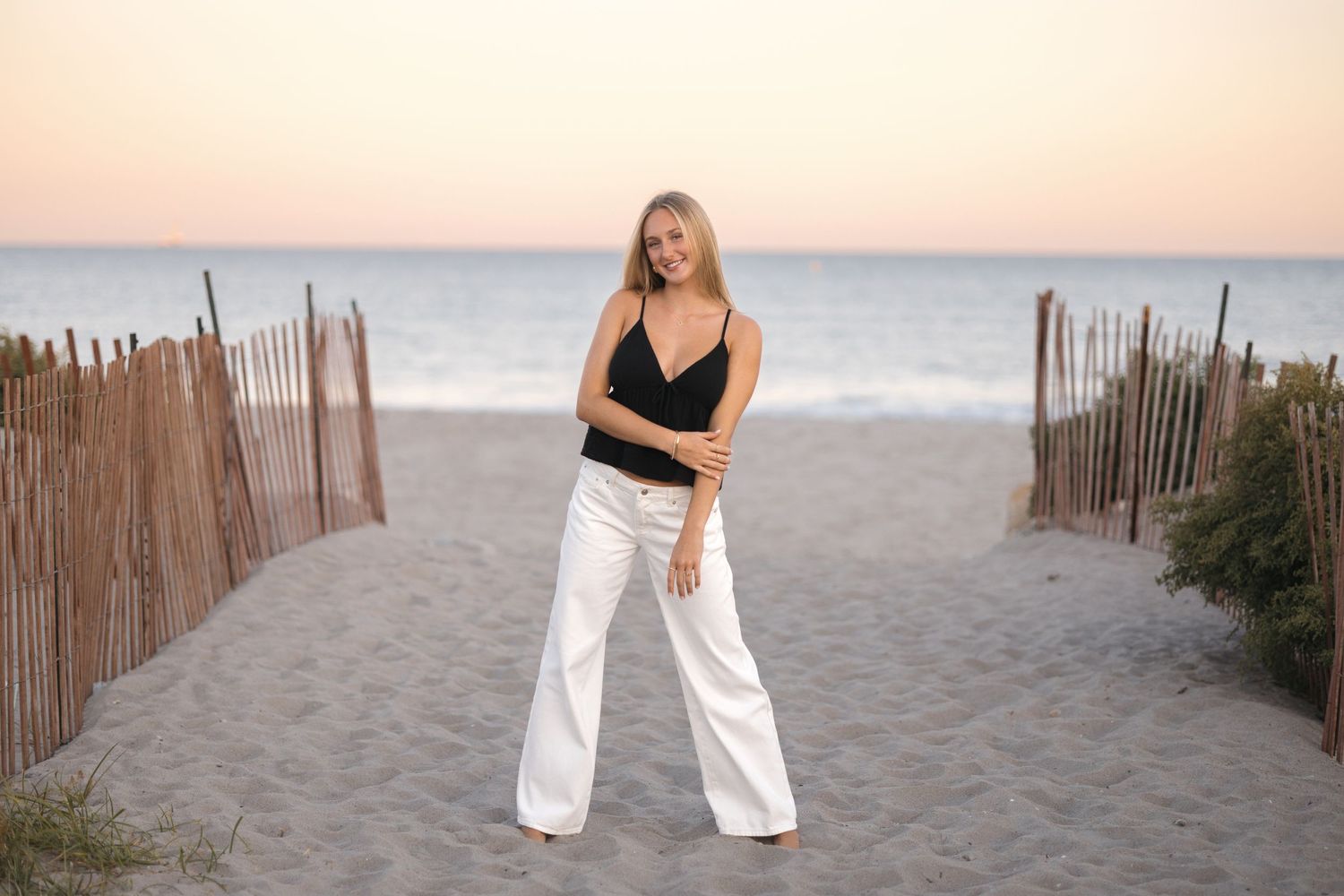 Beach fashion shoot with black top and white pants at golden hour.