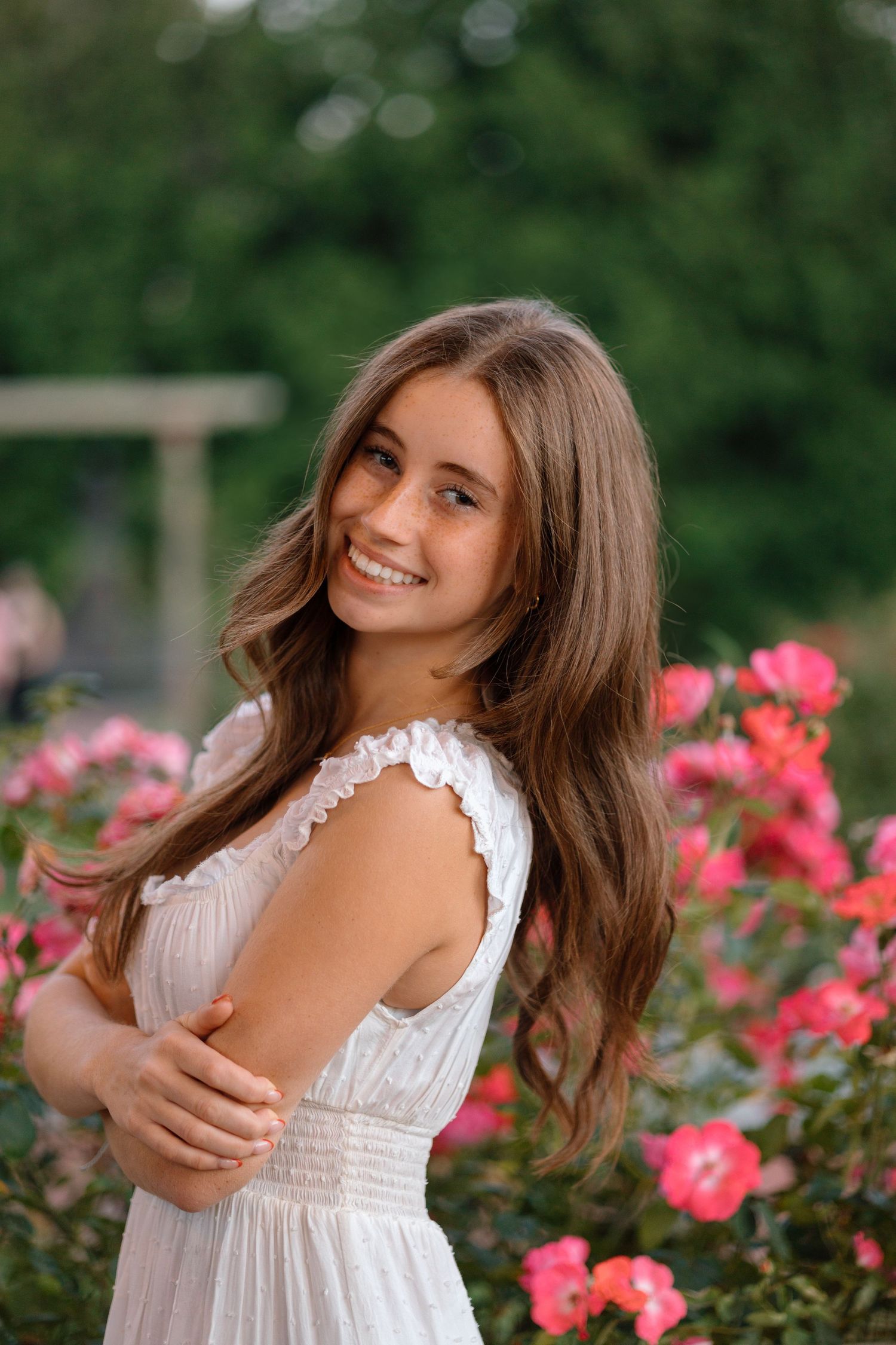 Portrait of woman in white dress standing among blooming pink roses in garden setting.