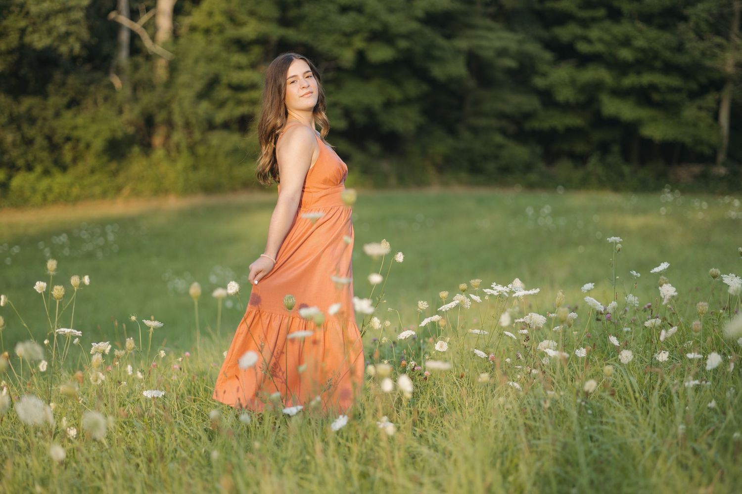 Person in flowing orange dress walking through field of wildflowers.